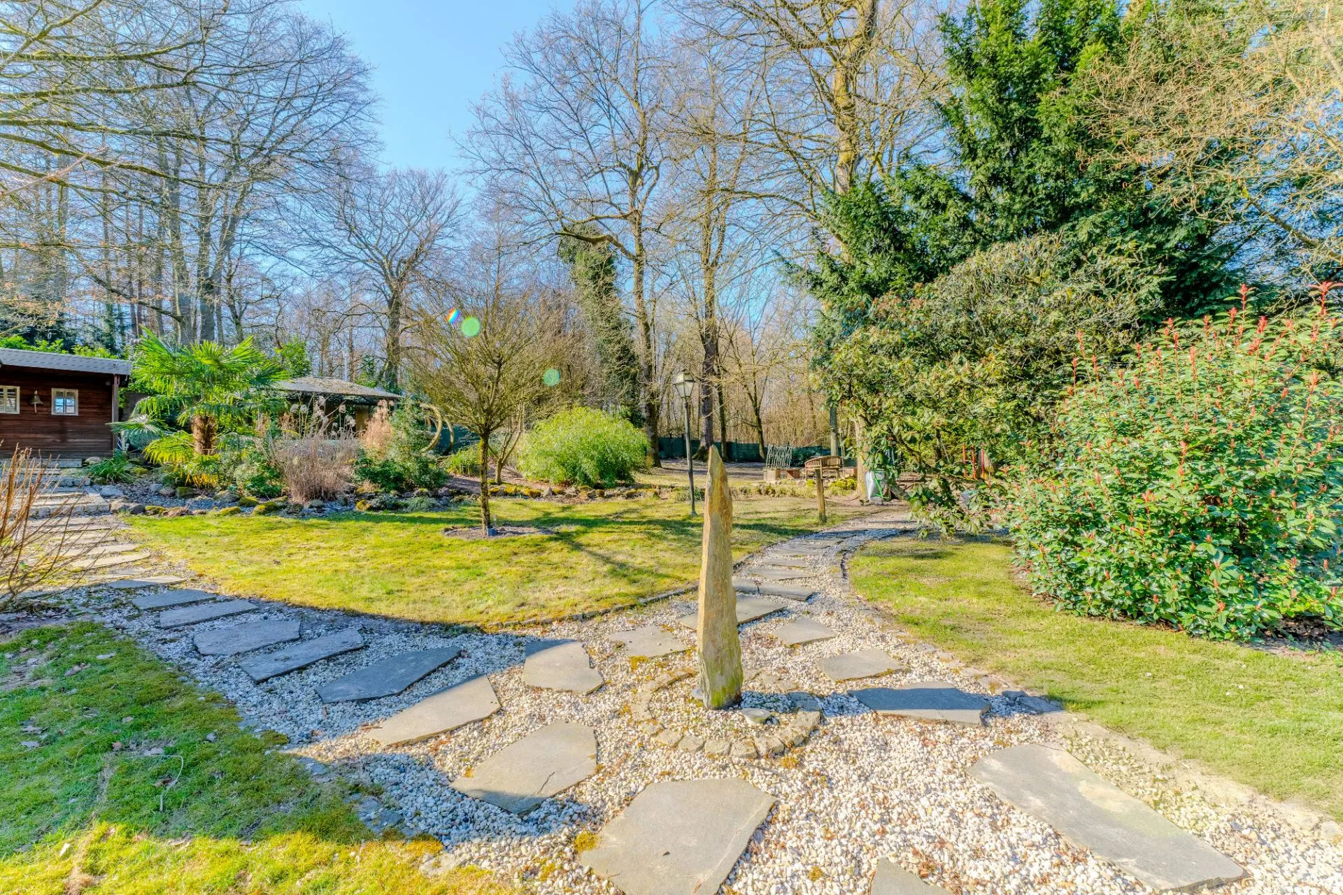 Gepflasterter Gartenweg führt durch einen großen Garten mit Bäumen und Sträuchern.