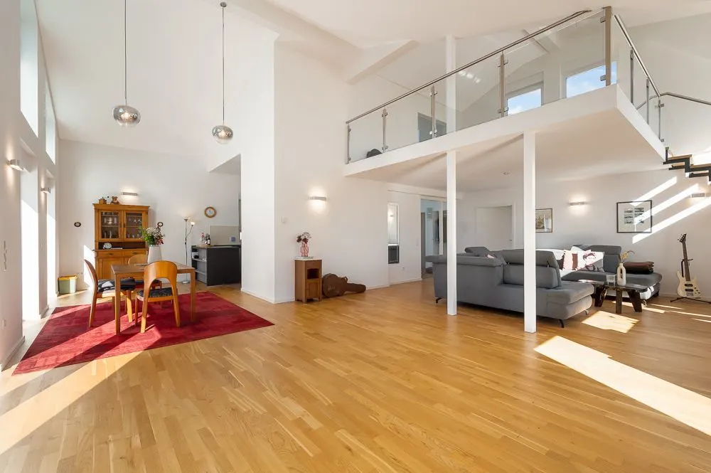 Helles Wohnzimmer mit Holzfußboden, Essbereich auf rotem Teppich, graue Sofas und Galerie.