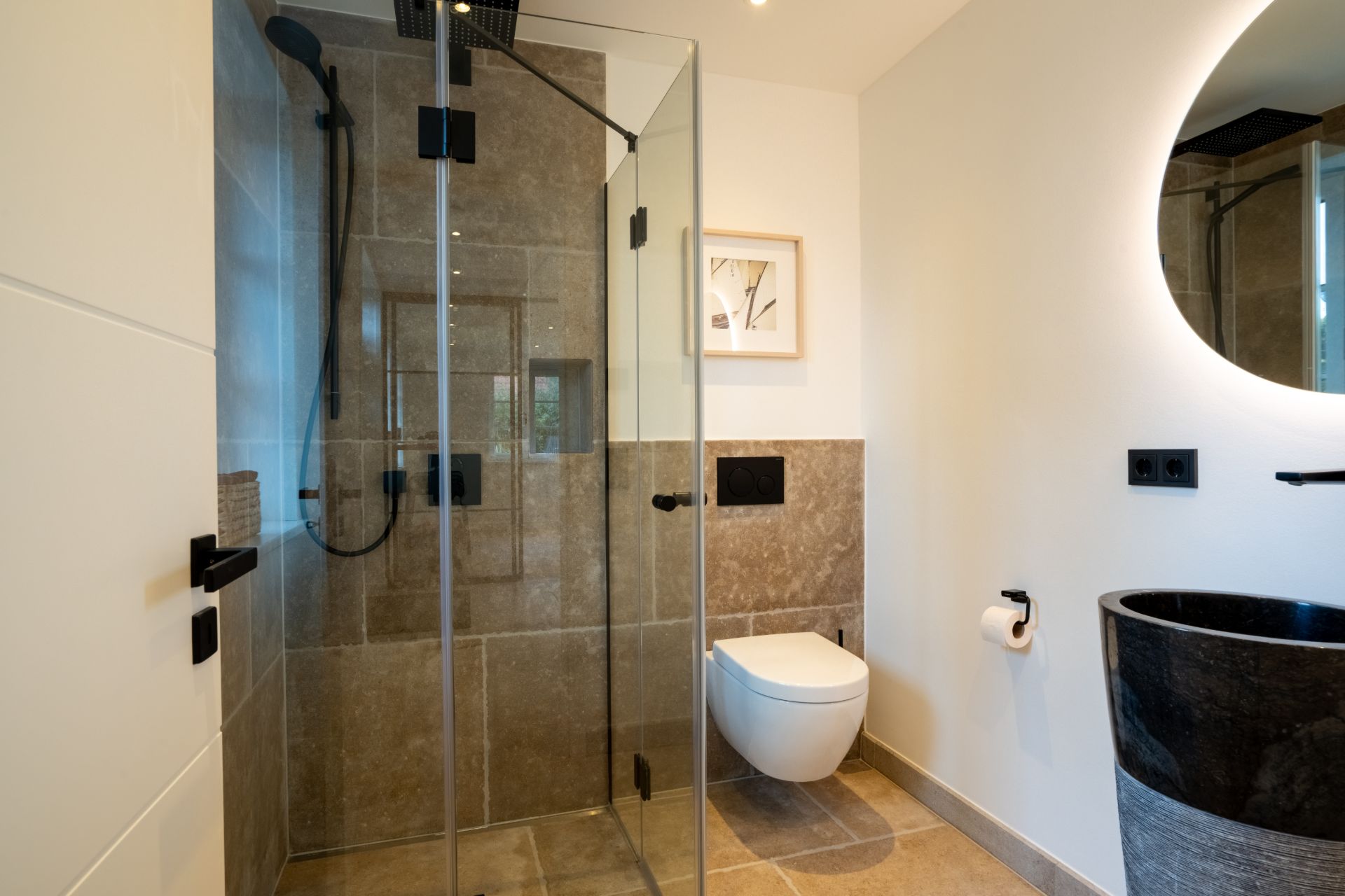 Modernes Bad mit Glasdusche, Hänge-WC, Waschbecken und rundem Spiegel.