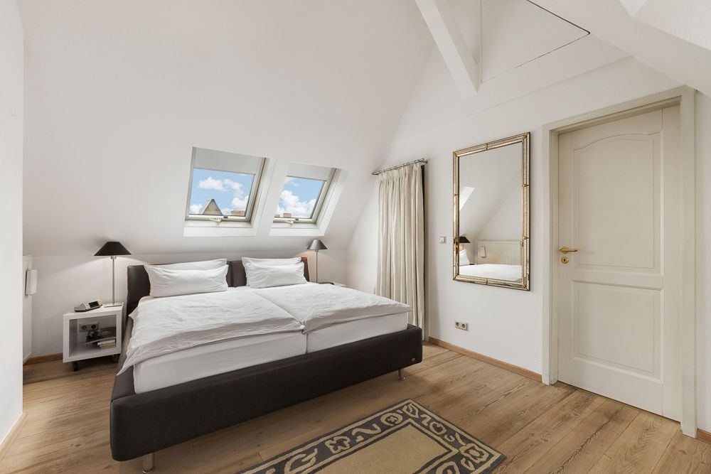 Helles Schlafzimmer mit Doppelbett, zwei Dachfenstern, Spiegel und Holzboden.