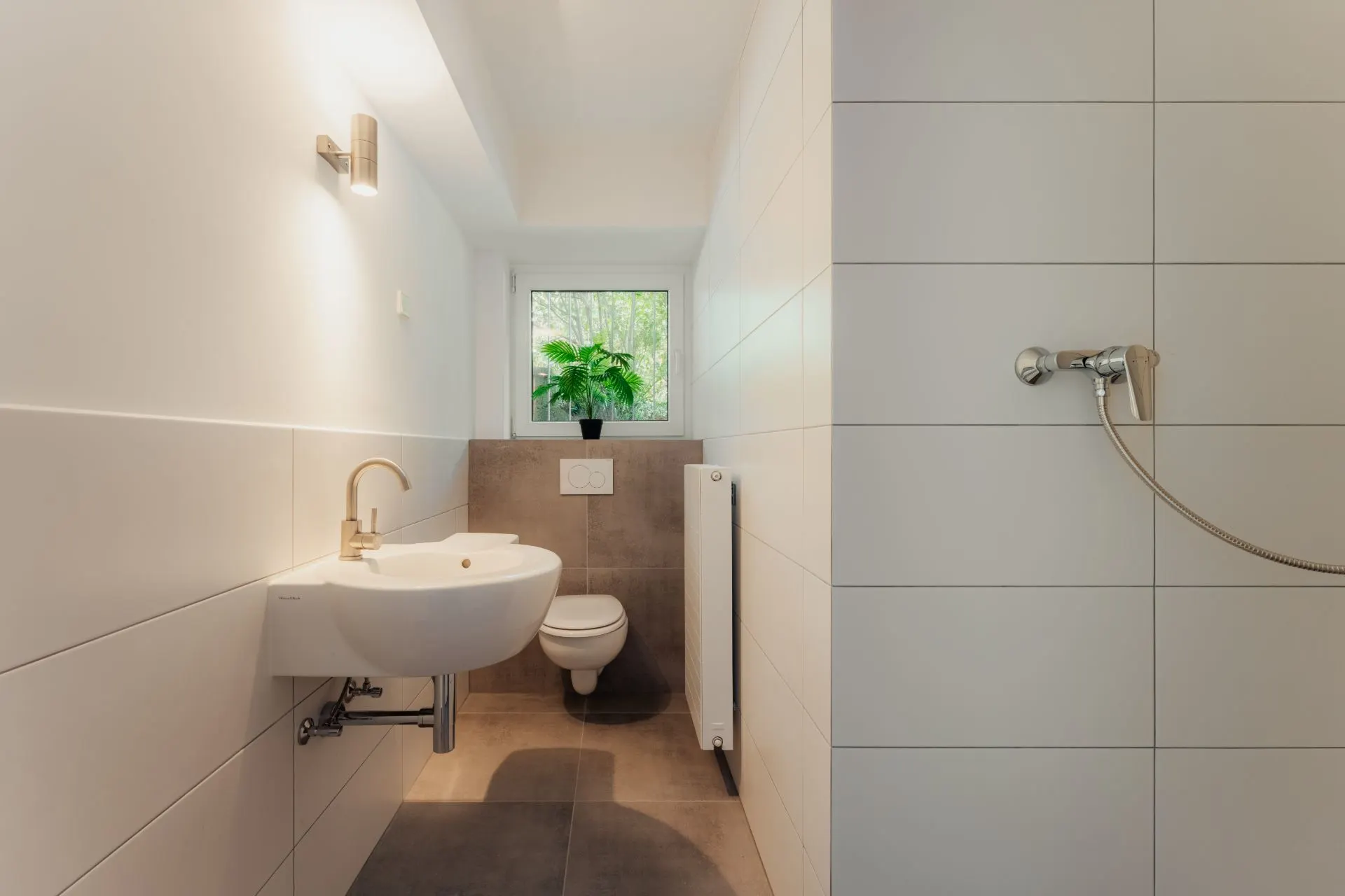 Modernes Badezimmer mit Waschbecken, WC, Dusche und einem Fenster mit Pflanze.