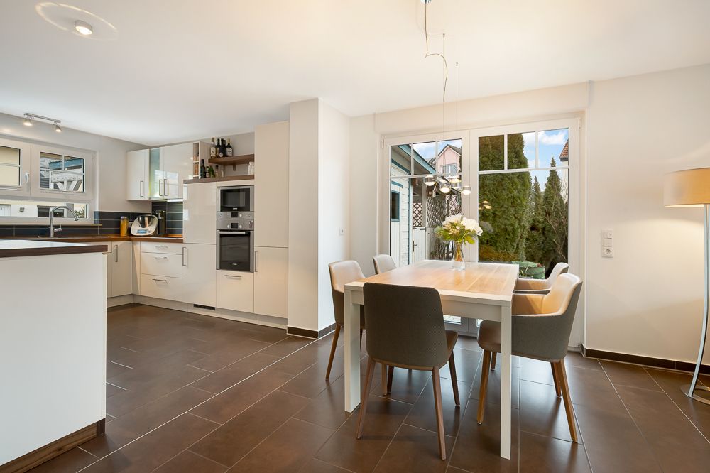 Helle Küche mit Essbereich, großem Fenster und sechs Stühlen um einen Holztisch.