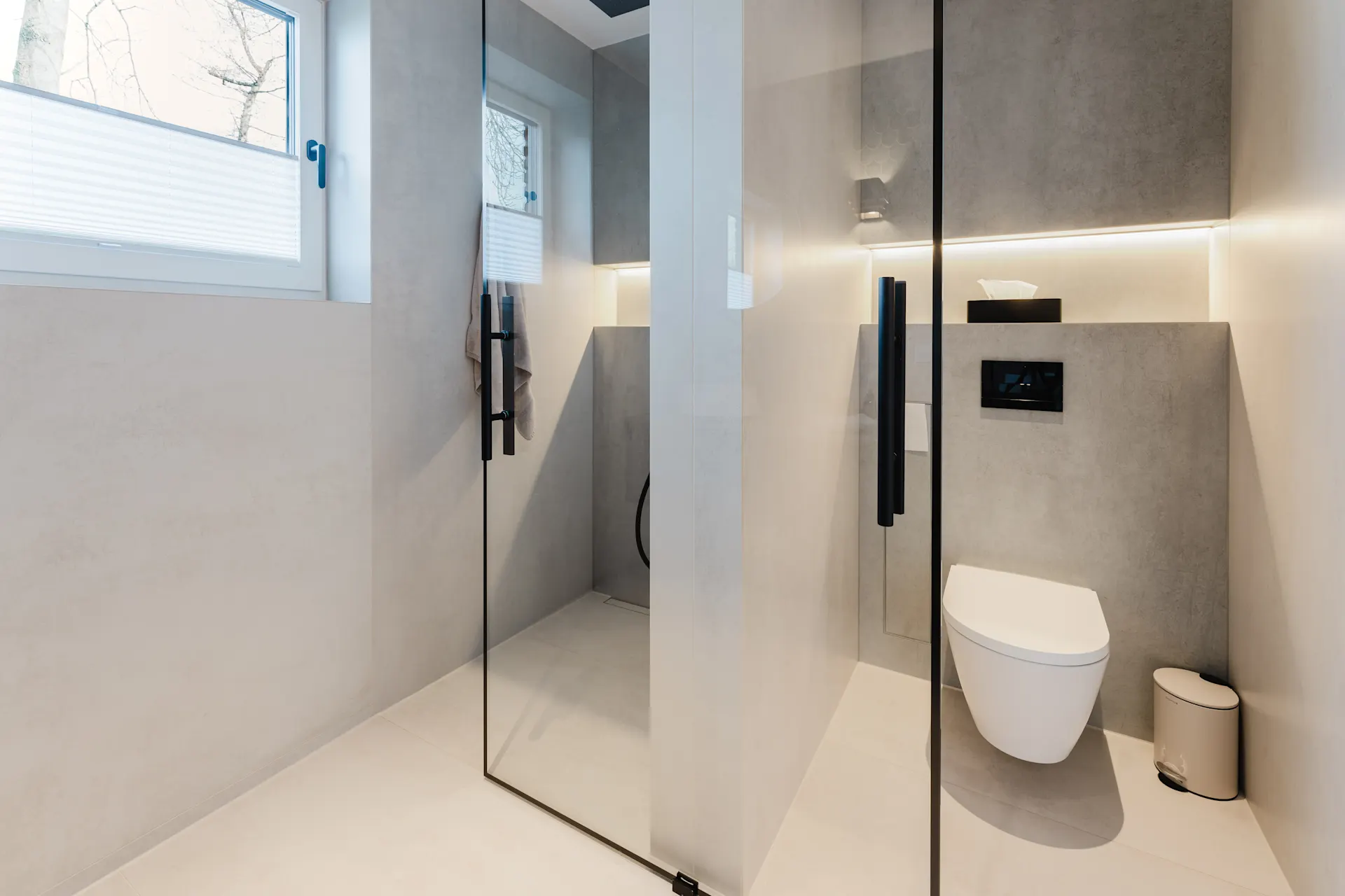 Modernes Badezimmer mit bodengleicher Dusche, Wandtoilette und großem Fenster.