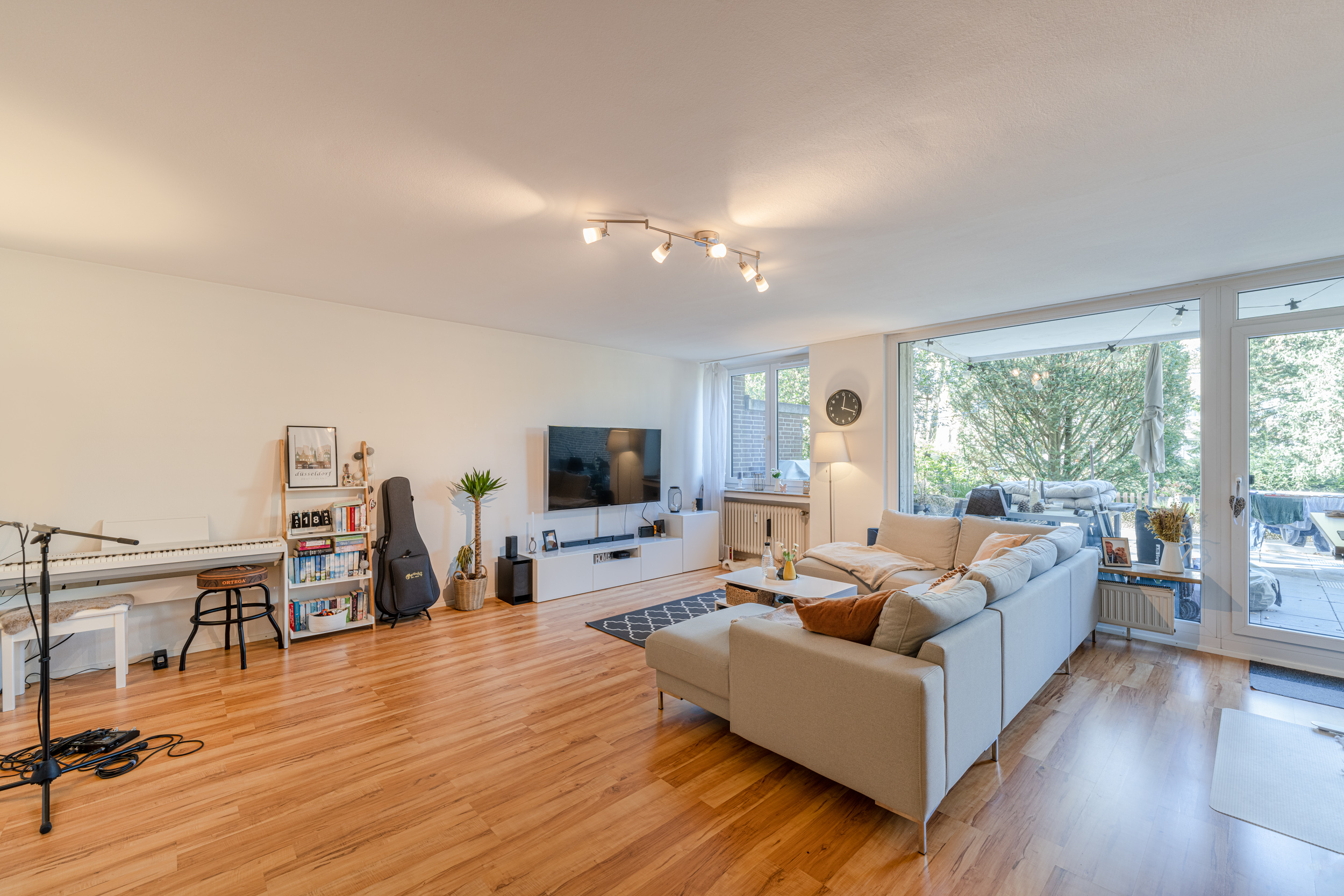 Helles Wohnzimmer mit Sofa, Fernseher, Klavier und Zugang zur Terrasse mit Gartenblick.