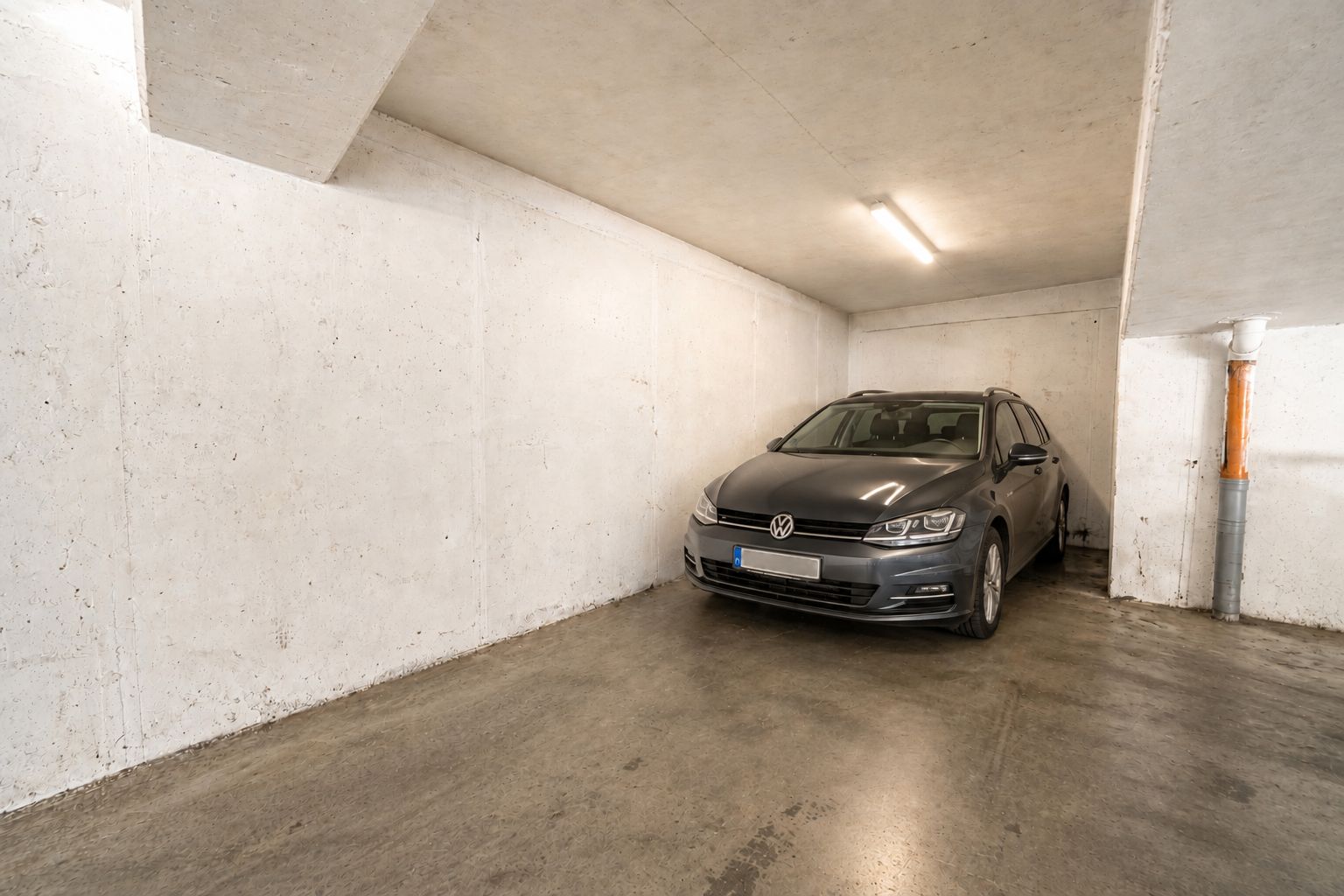 Graues Auto steht in einem beleuchteten Garagenstellplatz mit Betonwänden.