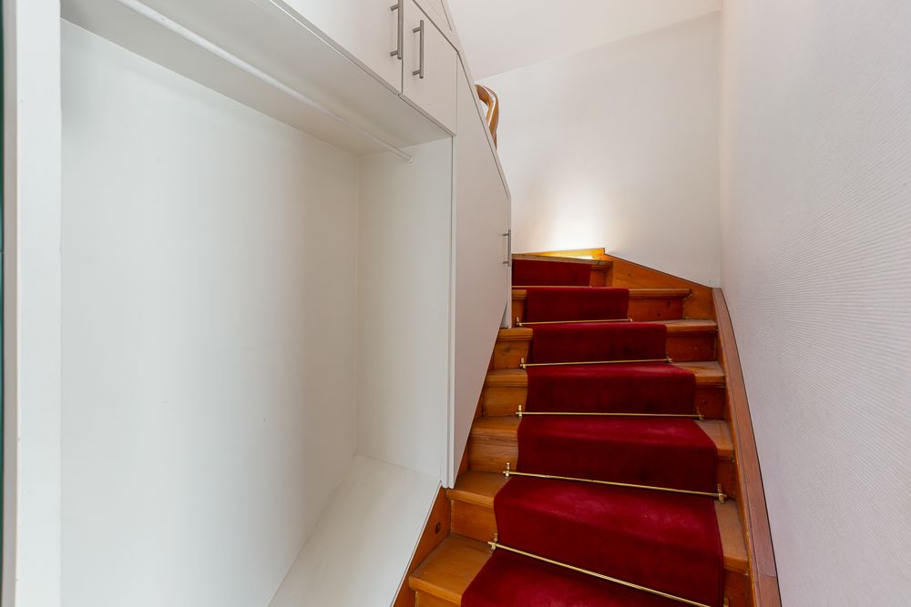 Holztreppe mit rotem Teppichläufer und weißem Einbauschrank an der Seite.