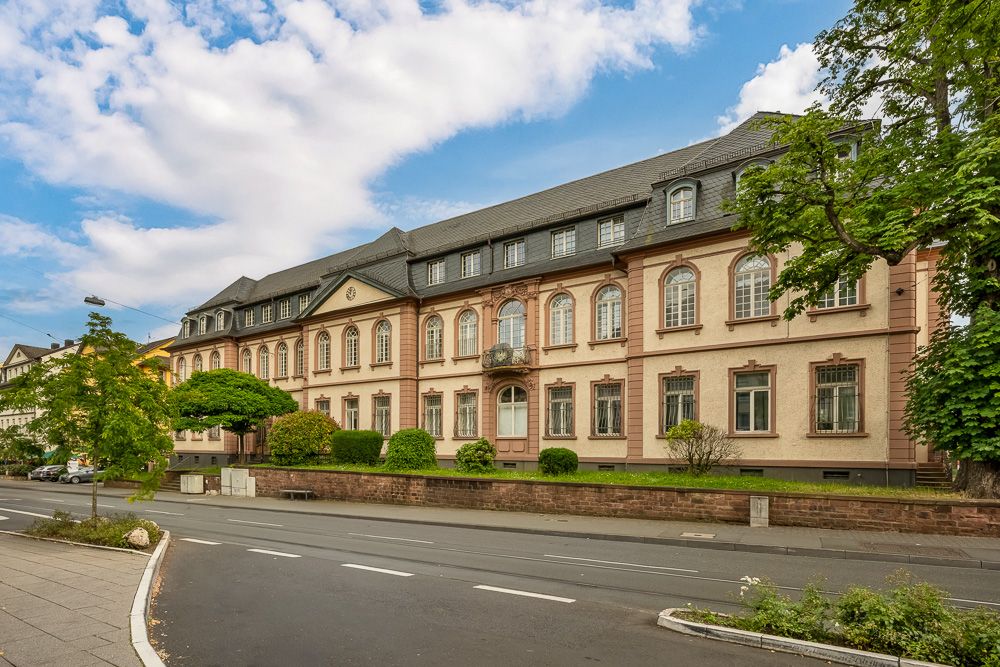 Großes, mehrstöckiges Wohngebäude mit historische Fassade und gepflegten Vorgarten an einer Straße.
