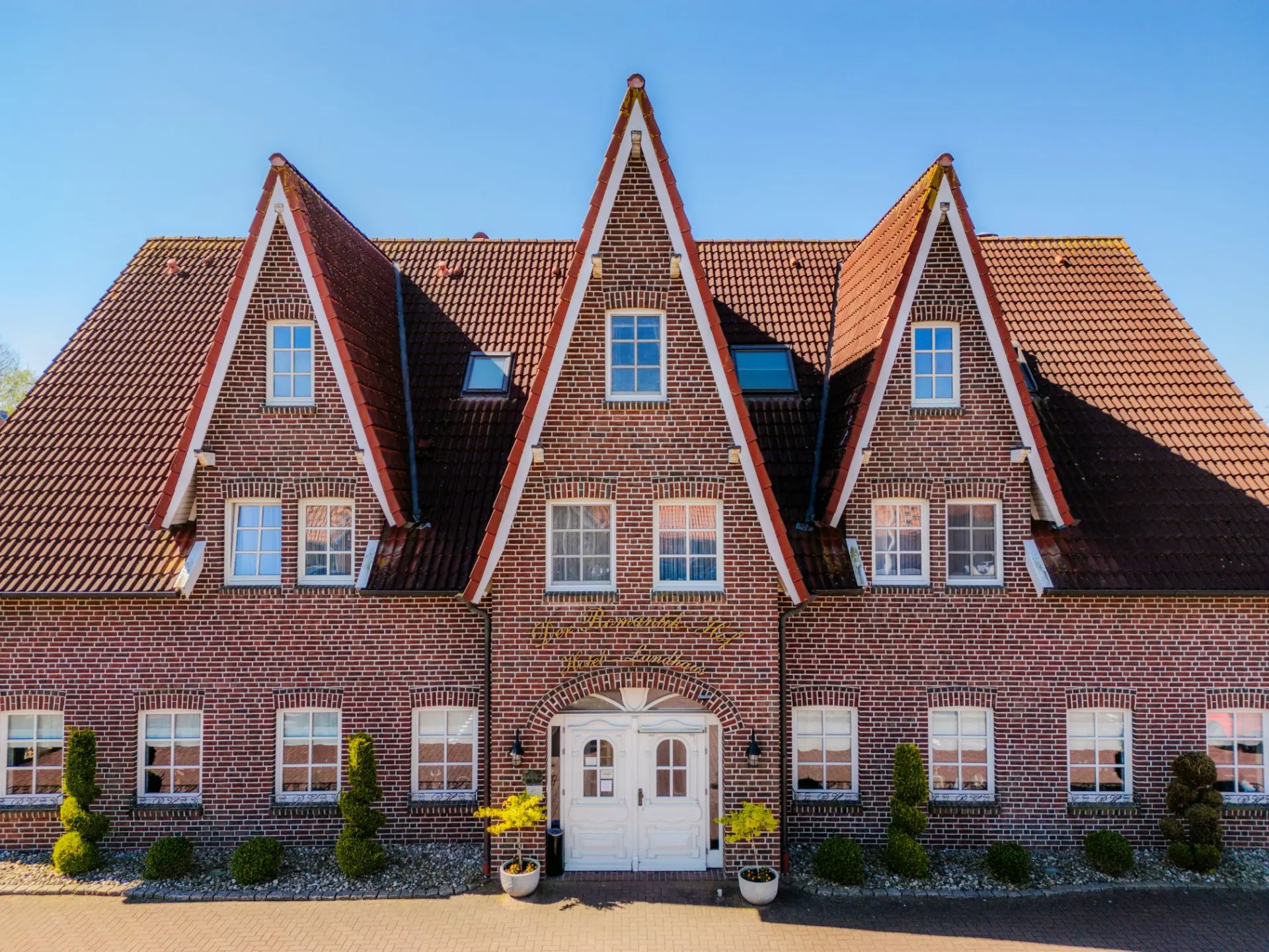 Backsteingebäude mit roten Giebeldächern, weißen Fenstern und einem weißen Eingangstor.
