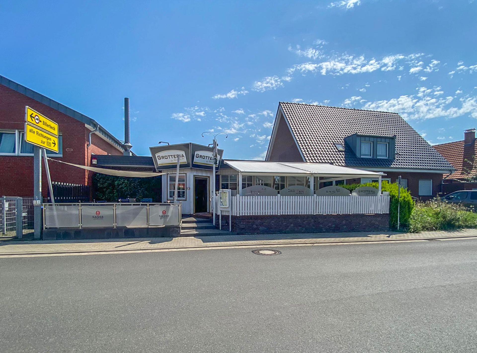 Zweistöckiges Wohnhaus mit Terrasse und Garten, Straßenansicht bei blauem Himmel.
