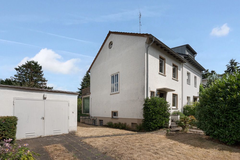 Weißes Wohnhaus mit Garten, Garage links und gepflastertem Weg im Vordergrund.