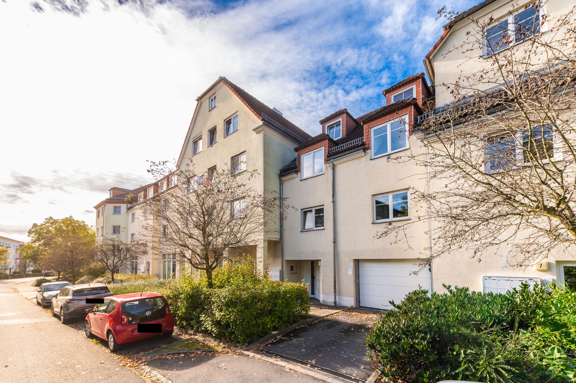 Mehrfamilienhaus mit hellen Fassaden und geparkten Autos entlang einer ruhigen Straße.