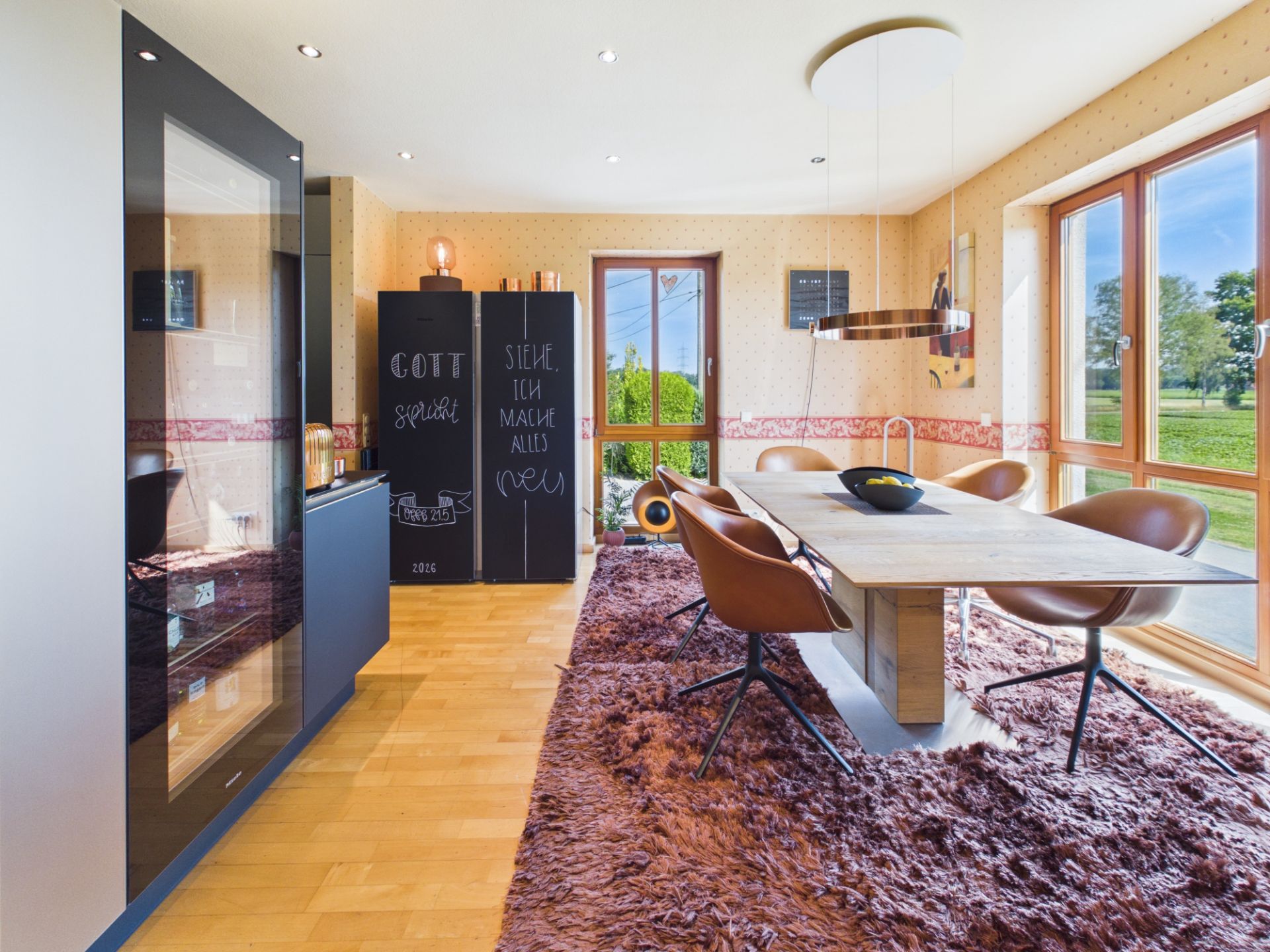 Esszimmer mit Holztisch, braunen Stühlen, großen Fenstern und braunem Teppich.
