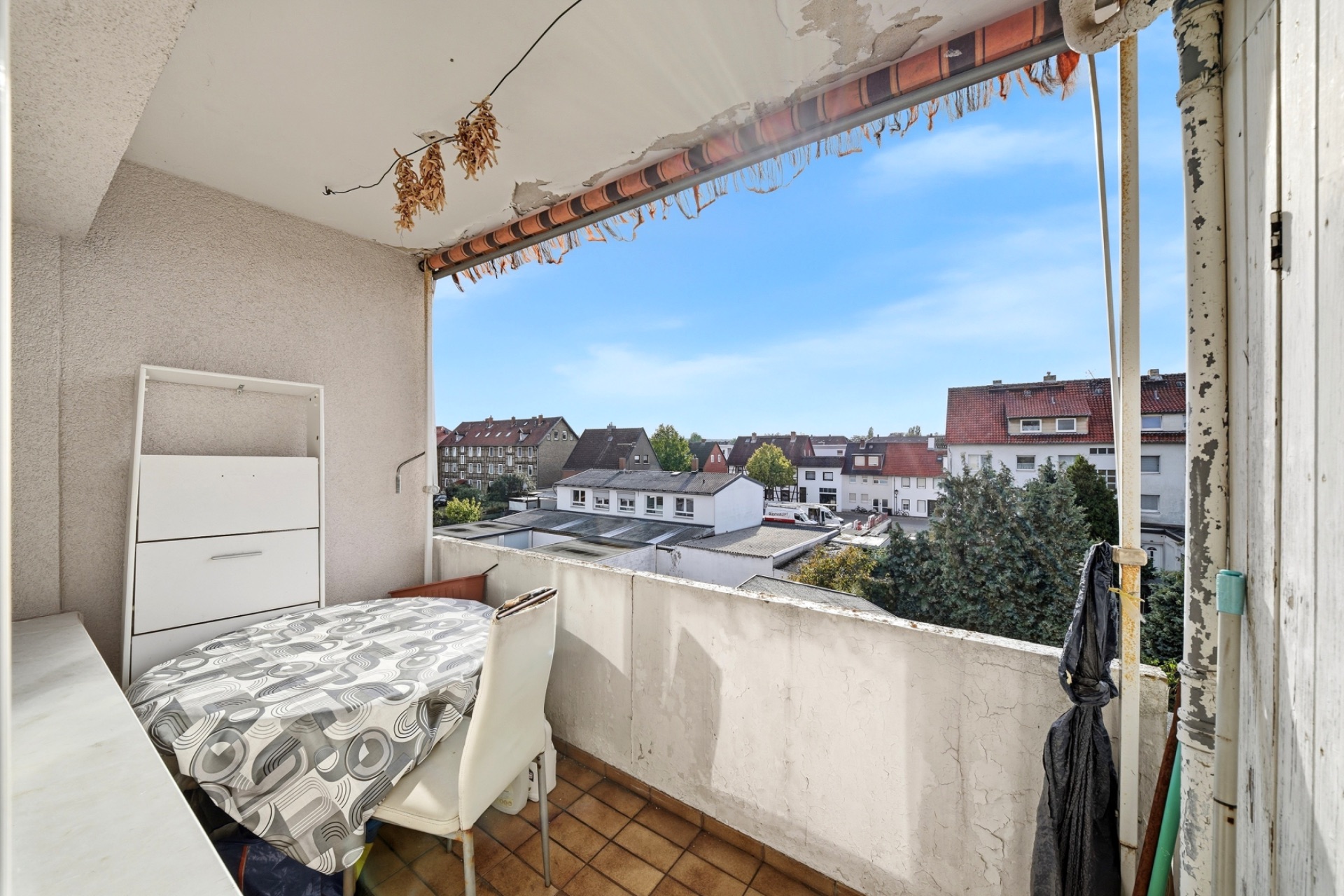 Balkon mit Tisch, zwei Stühlen und Blick auf Wohnhäuser unter blauem Himmel.
