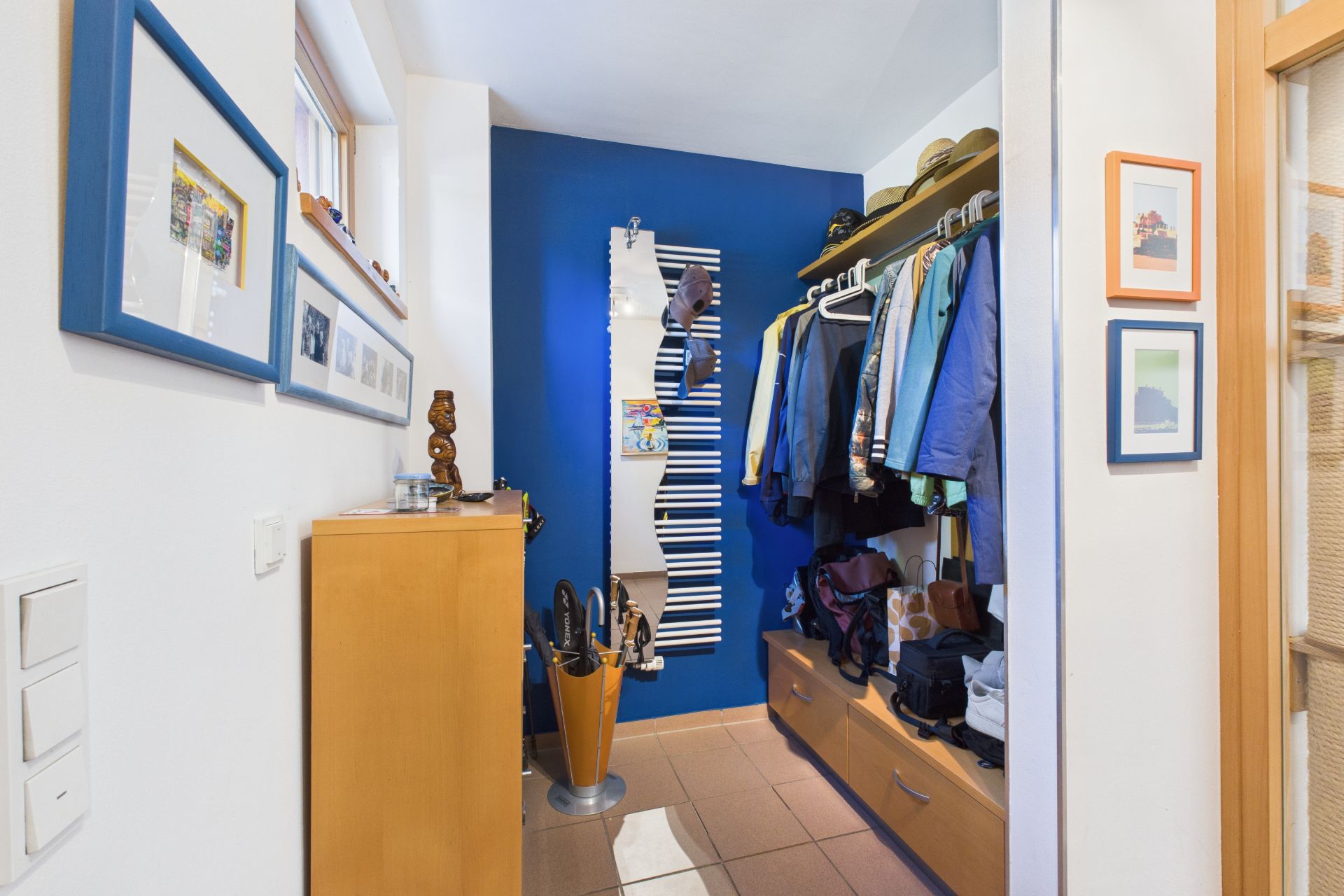 Flur mit blau gestrichener Wand, Spiegel, Garderobe mit Jacken und Schirmständer.