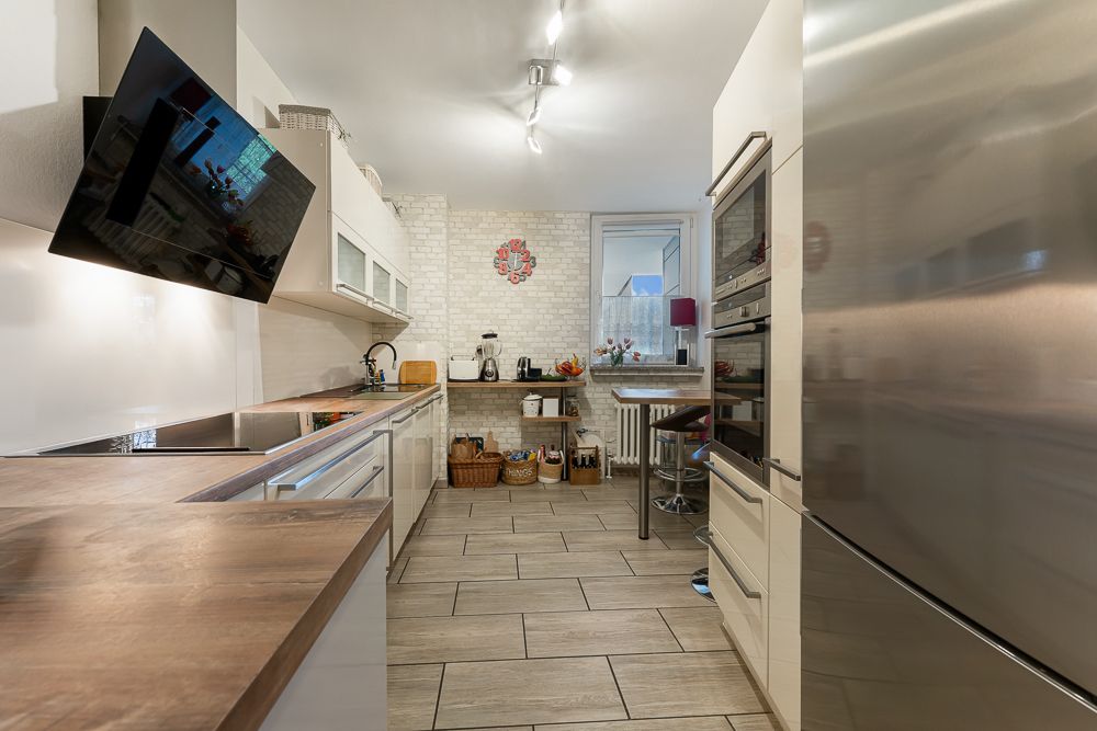 Moderne Küche mit Holzarbeitsplatte, großem Kühlschrank und Wandfernseher, Blick zum Fenster.