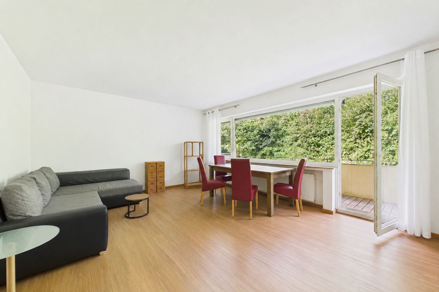 Helles Wohnzimmer mit Ecksofa, Esstisch, roten Stühlen und großen Fenstern zur Terrasse.