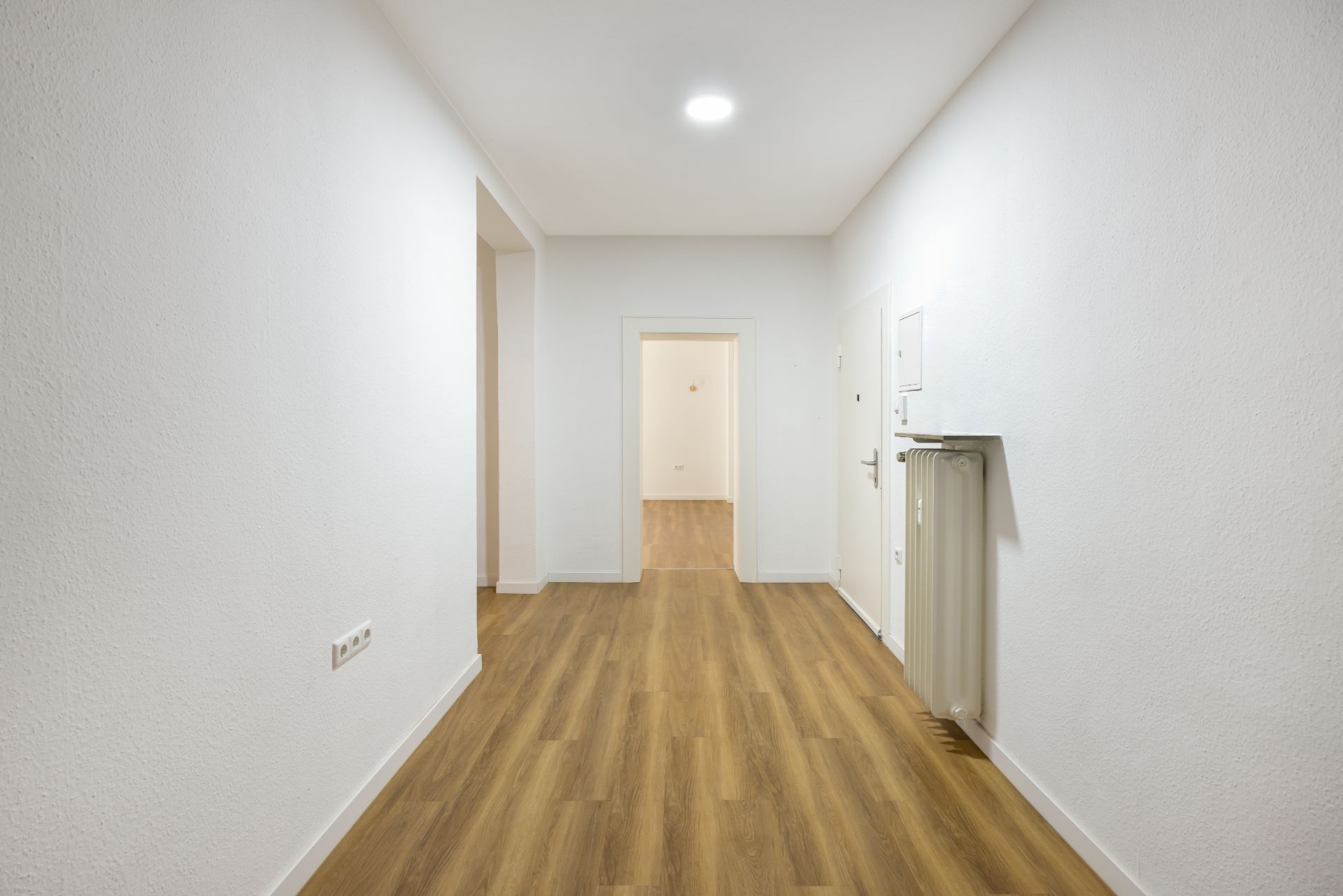 Heller Flur mit Holzfußboden, weißen Wänden und Deckenleuchte, Türen führen zu weiteren Räumen.