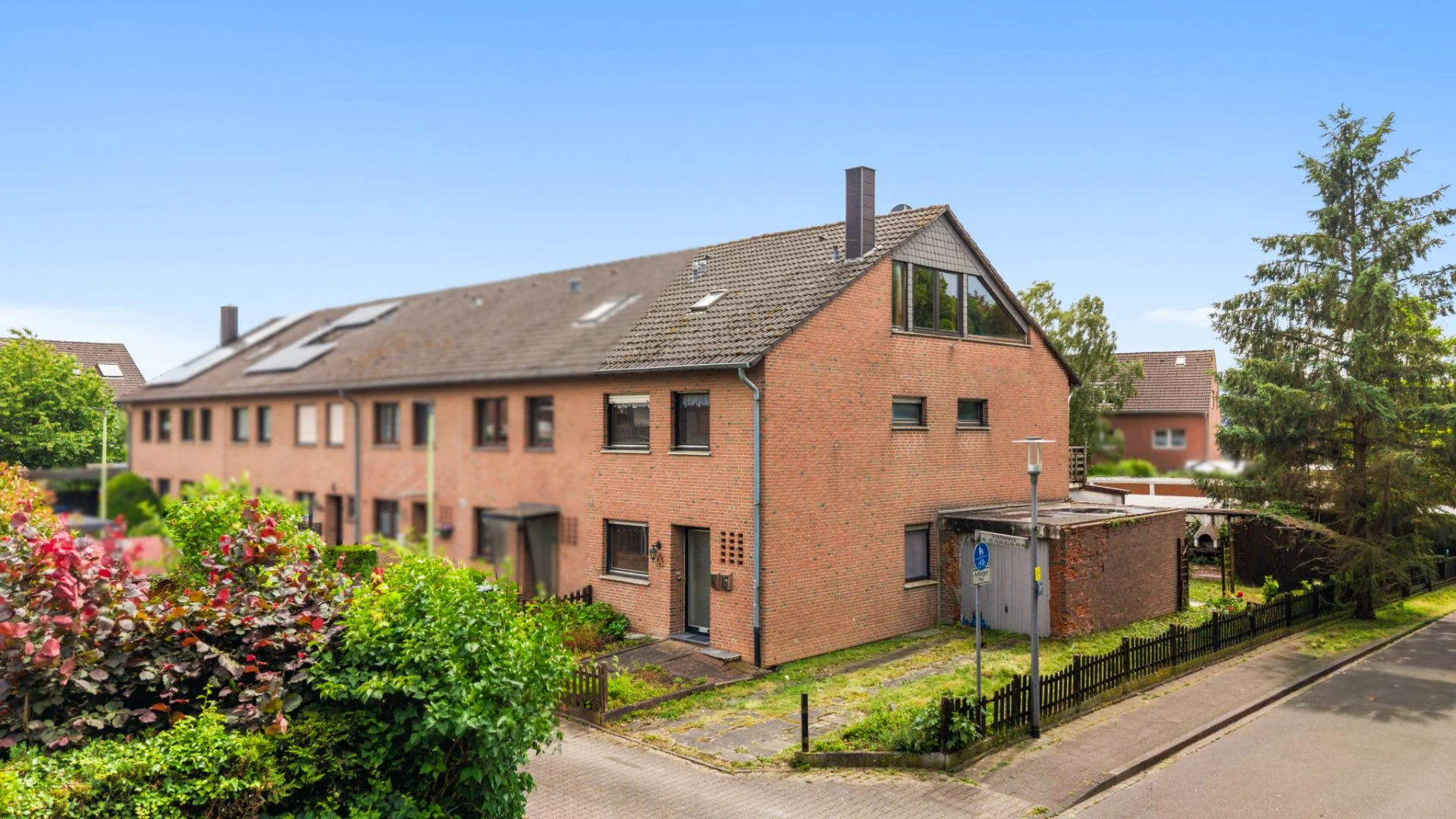 Mehrfamilienhaus aus rotem Backstein mit mehreren Fenstern und Vorgärten an einer ruhigen Straße.