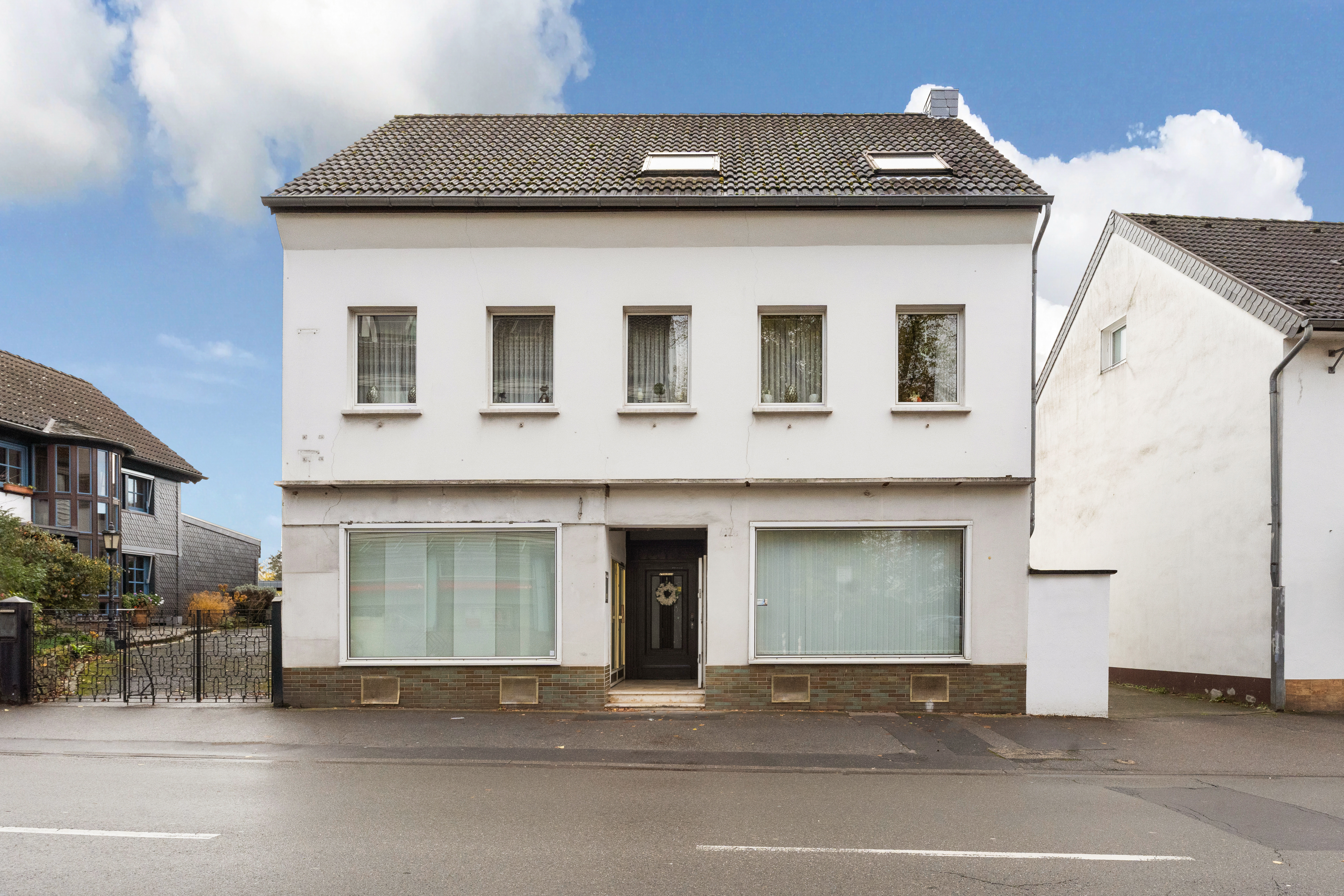Zweistöckiges weißes Wohnhaus mit vier Fenstern oben und zwei großen Fenstern im Erdgeschoss.