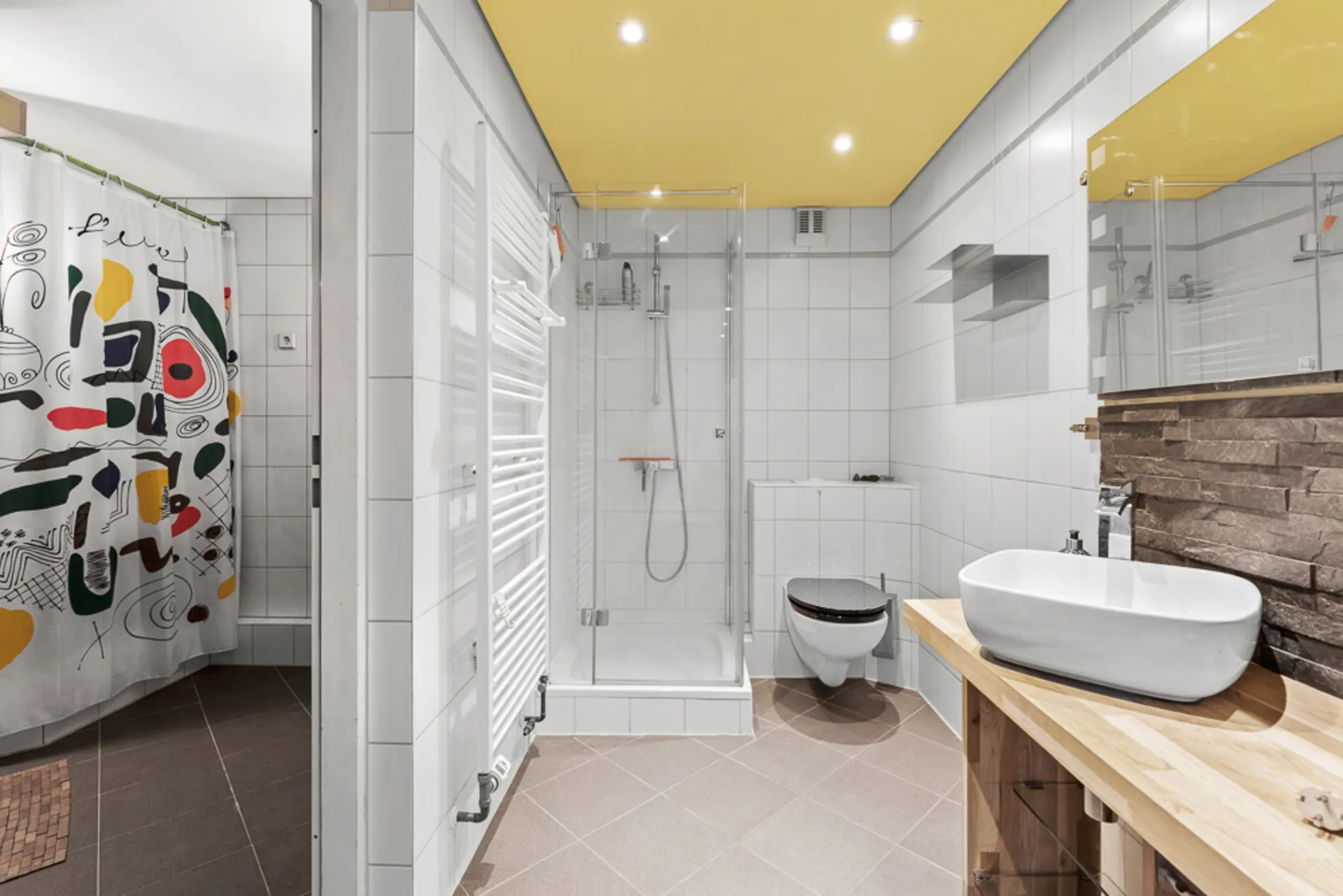 Modernes Bad mit Dusche, Wand-WC, Waschbecken und bunter Duschvorhang.