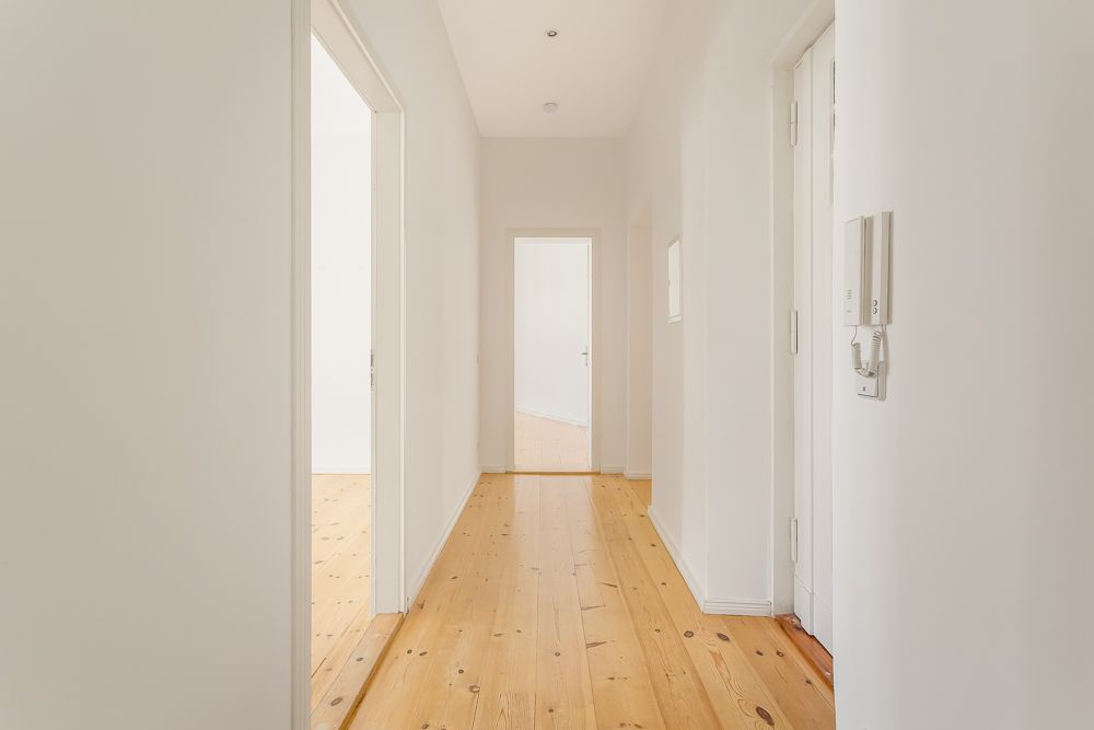 Heller Flur mit Holzboden und weißen Wänden, mehrere Türen führen in andere Räume.