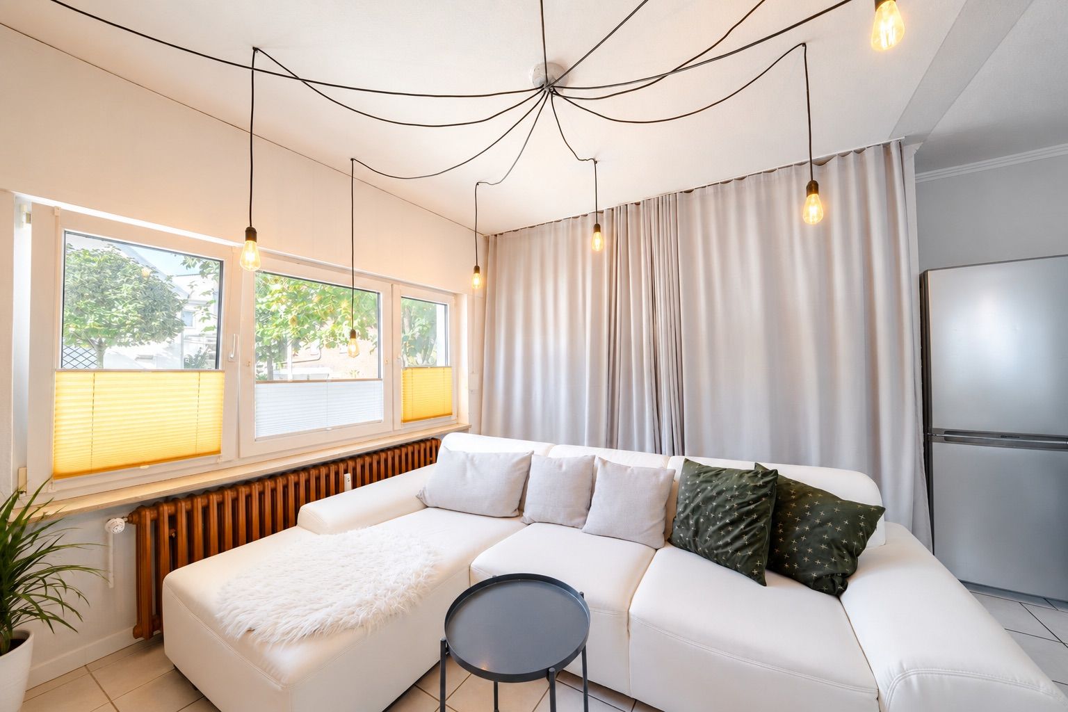Helles Wohnzimmer mit weißem Sofa, Rundtisch, großen Fenstern und modernen Hängelampen.