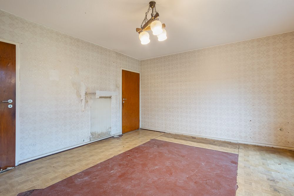 Leerer Raum mit Holzfußboden, abgenutztem Teppich, zwei Holztüren und Deckenlampe.