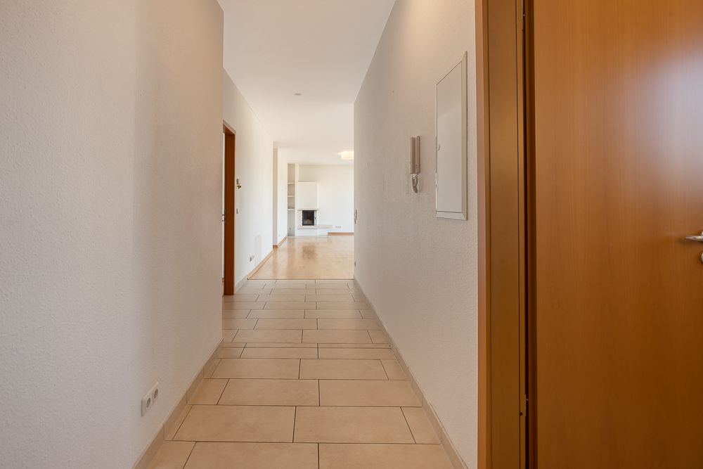 Heller Flur mit Fliesenboden, der in ein Wohnzimmer mit Kamin führt.