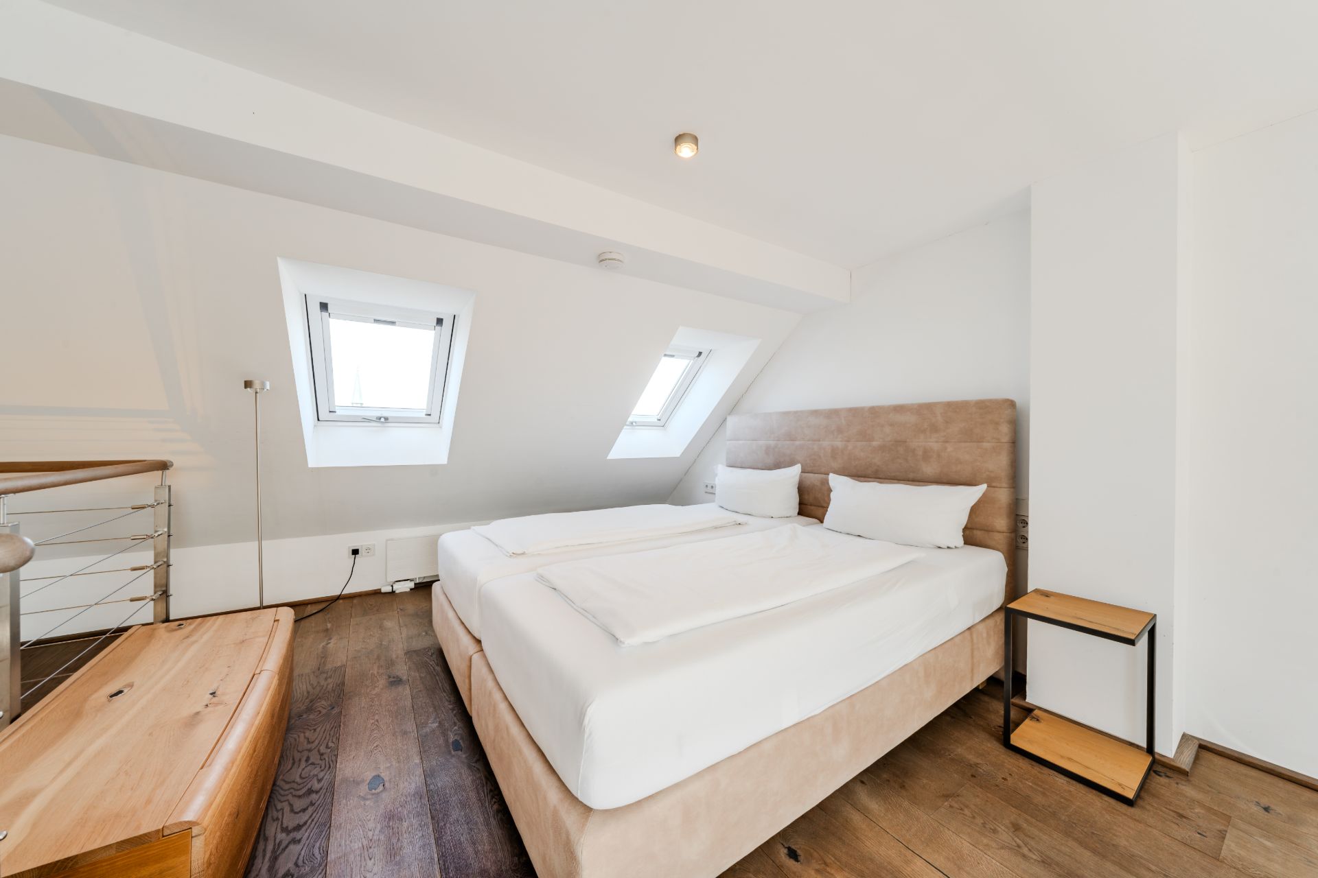 Schlafzimmer mit Doppelbett, Nachttisch und zwei Dachfenstern in einem hellen Raum.