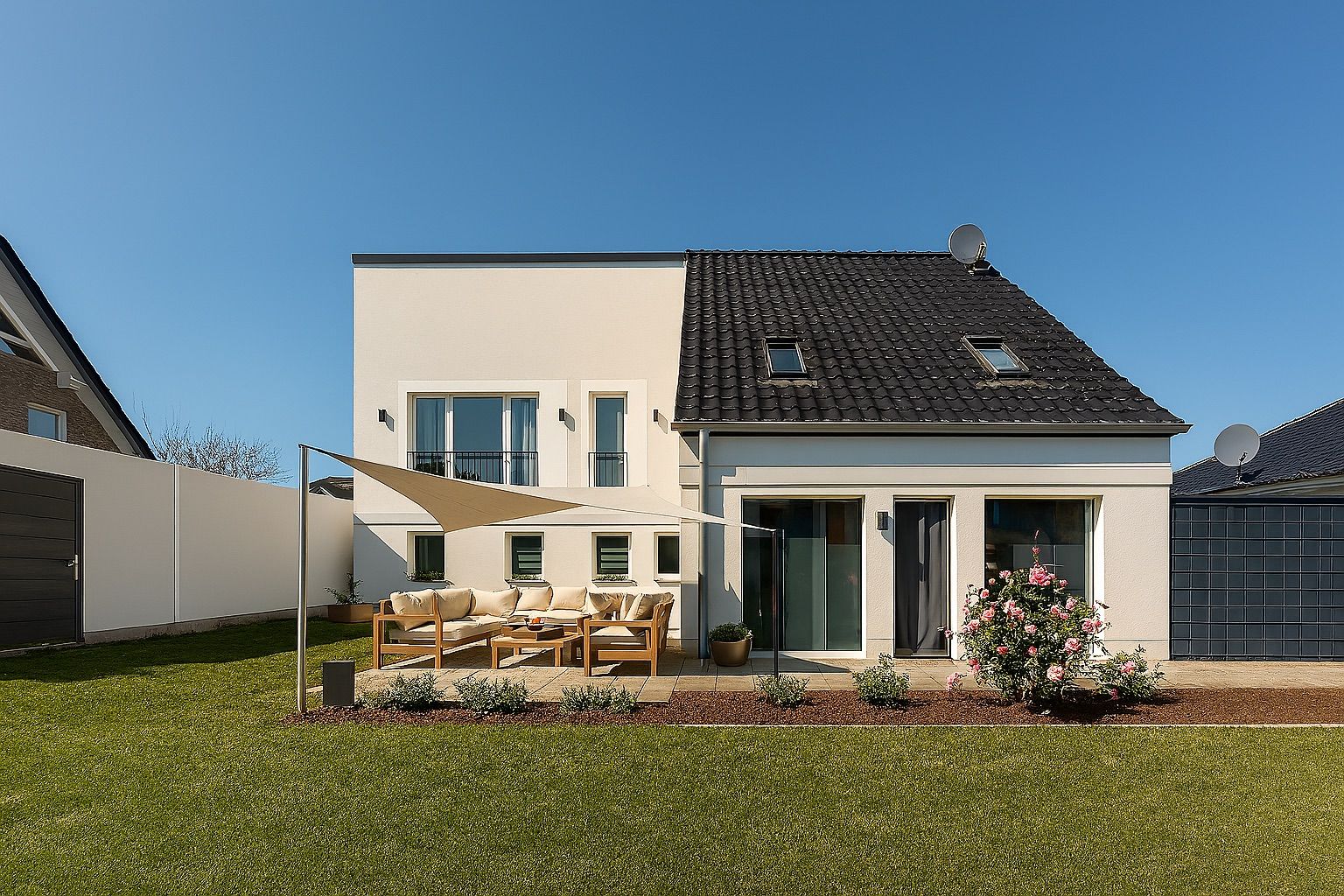 Modernes Einfamilienhaus mit Terrasse, Gartenmöbeln und Sonnensegel im Garten.