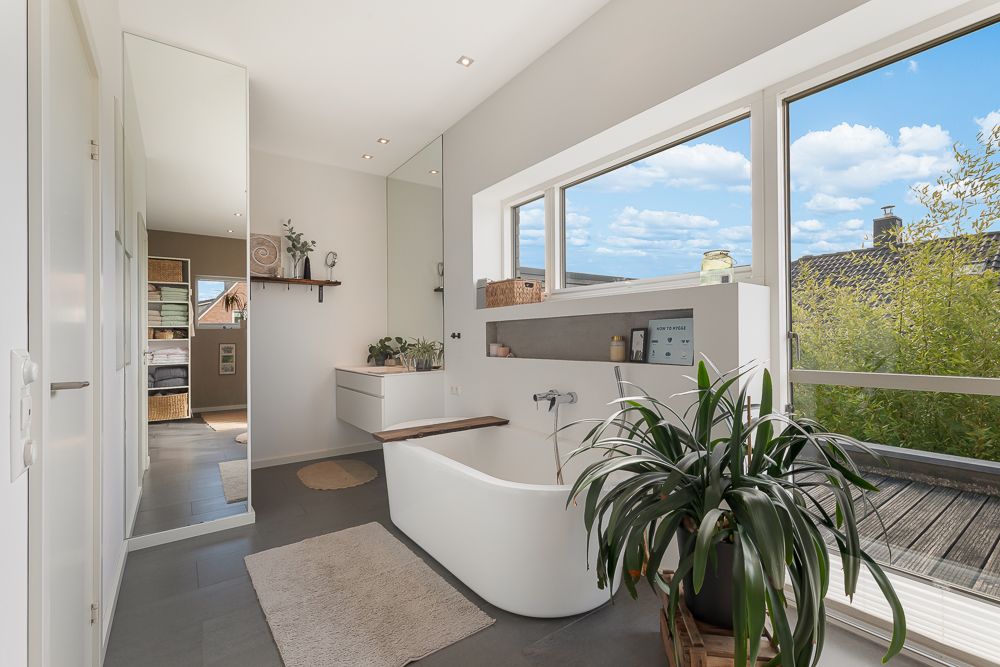 Modernes Badezimmer mit freistehender Badewanne, großen Fenstern und einer grünen Pflanze.