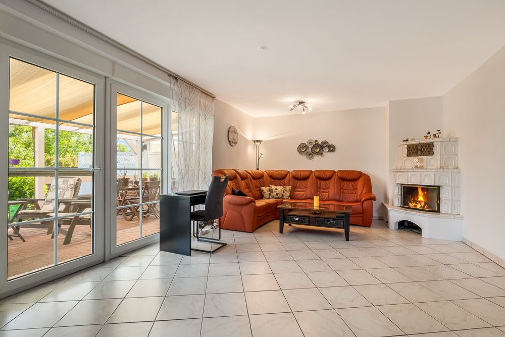 Wohnzimmer mit orangefarbener Eckcouch, Kamin, Couchtisch und Zugang zur Terrasse mit Gartensicht.