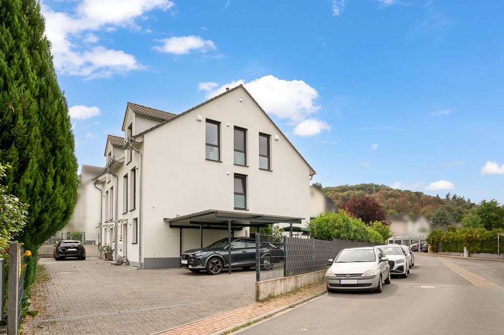 Modernes, weißes Wohngebäude mit mehreren Autos auf einer ruhigen Straße und Carport.