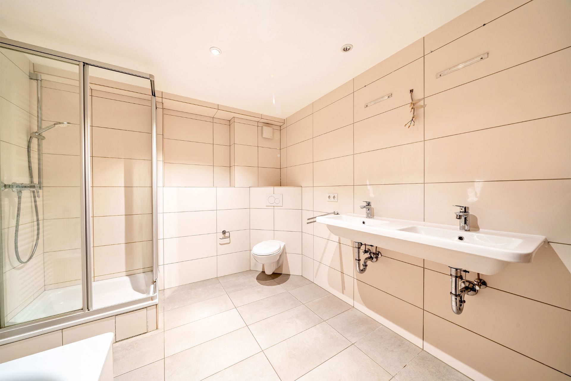 Modernes Badezimmer mit Dusche, Doppelwaschbecken und Wandtoilette, beige gefliest.