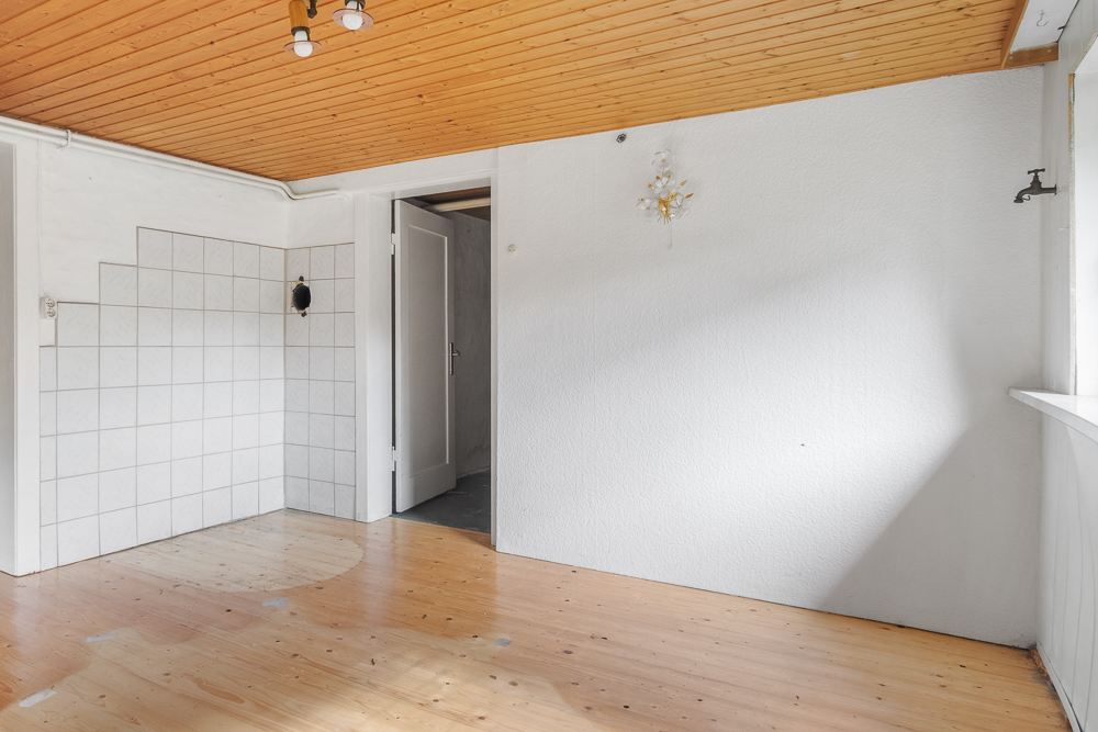 Leerer Raum mit Holzboden, weißer Wand, Holzdecke und Fliesenecke.
