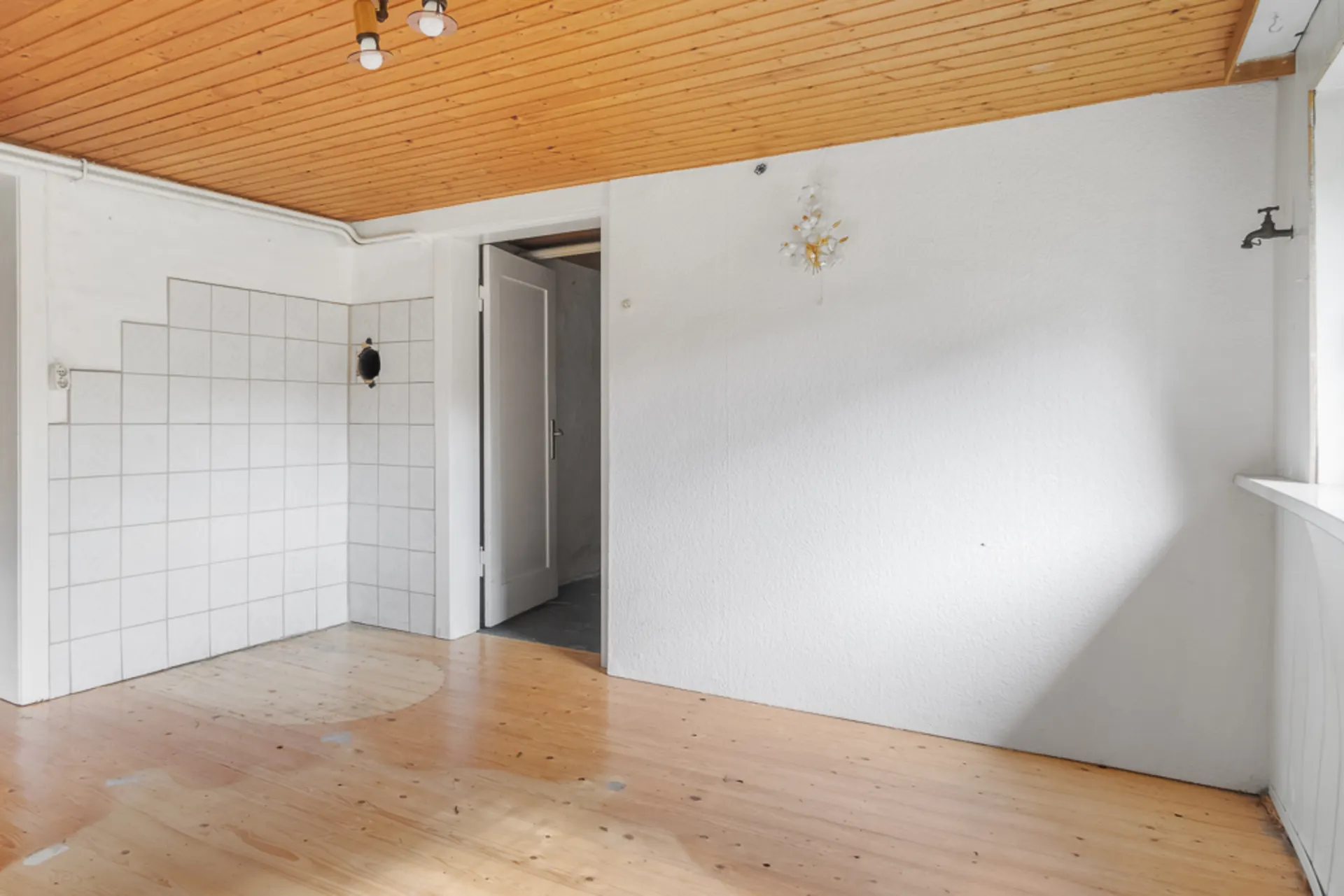 Leerer Raum mit Holzboden, weißer Wand, Holzdecke und Fliesenecke.