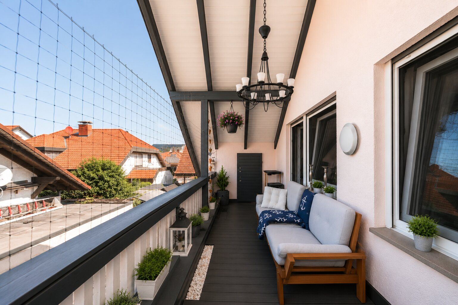 Überdachter Balkon mit Sofa, Pflanzen, Geländer und Blick auf Nachbarhäuser.