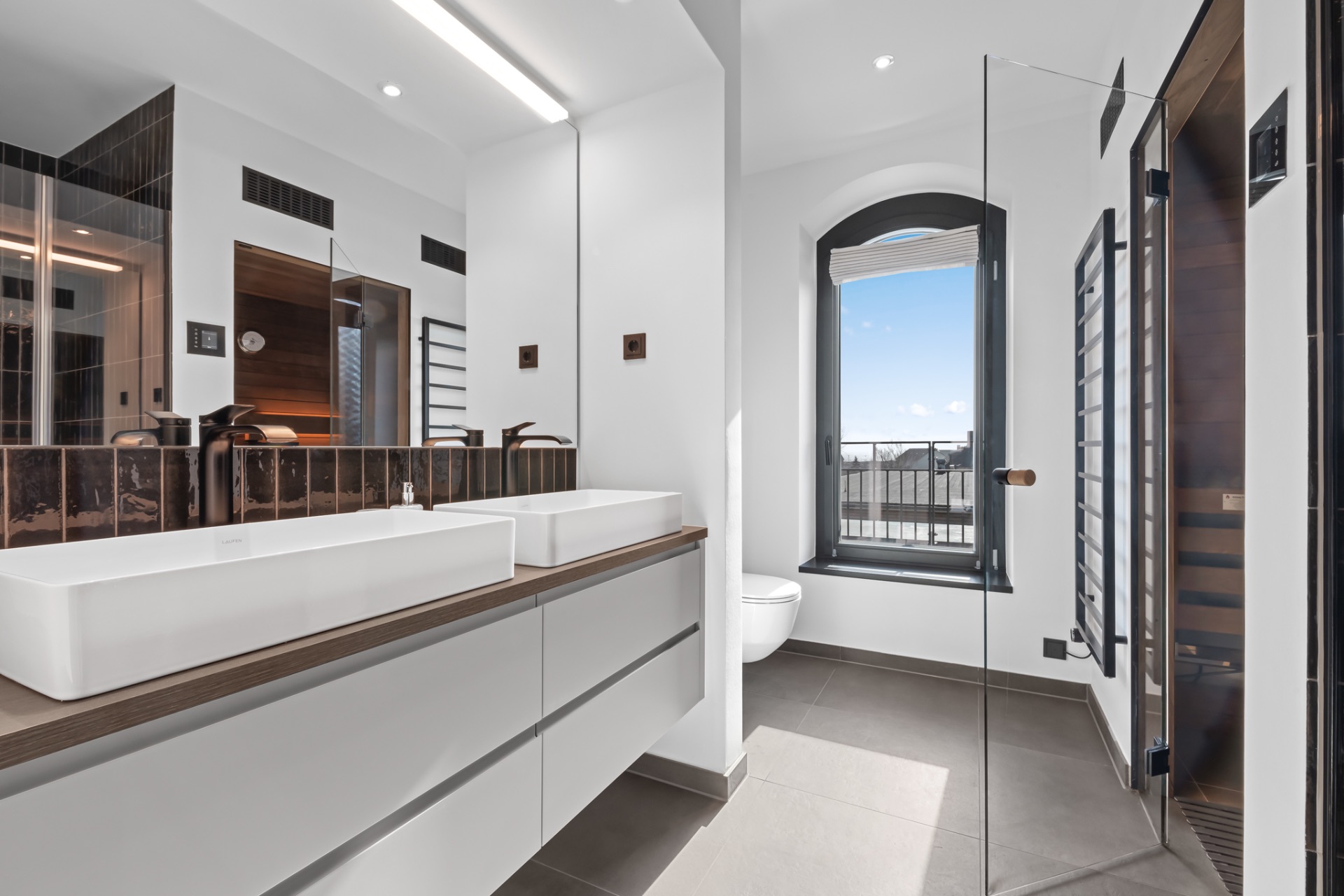 Modernes Badezimmer mit zwei Waschbecken, großem Spiegel, Fenster und Dusche mit Glastür.