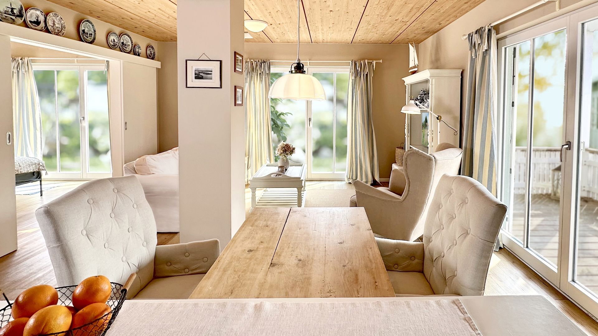 Helles Wohnzimmer mit Esstisch, Polsterstühlen, Sofa und großen Fenstern.