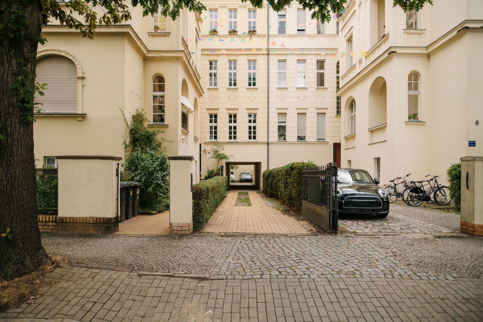 Einfahrt zu einem Wohngebäude mit offenem Tor, parkenden Autos und Fahrrädern rechts.