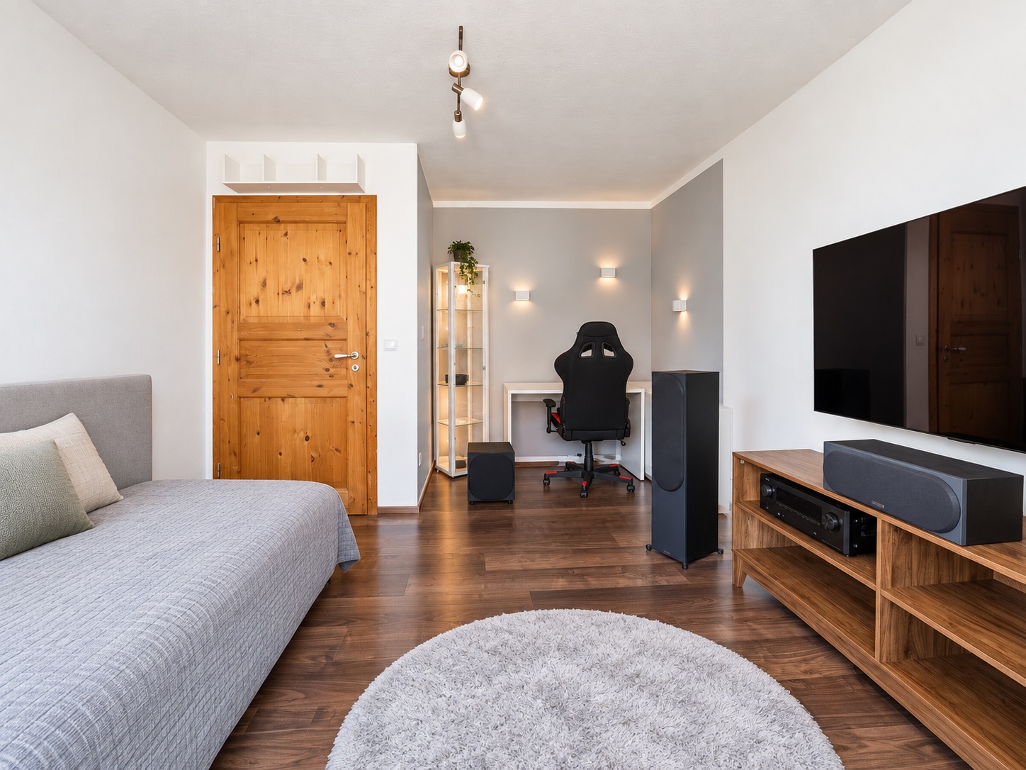 Modernes Zimmer mit Bett, Schreibtisch, Regal, TV und Holzfußboden.