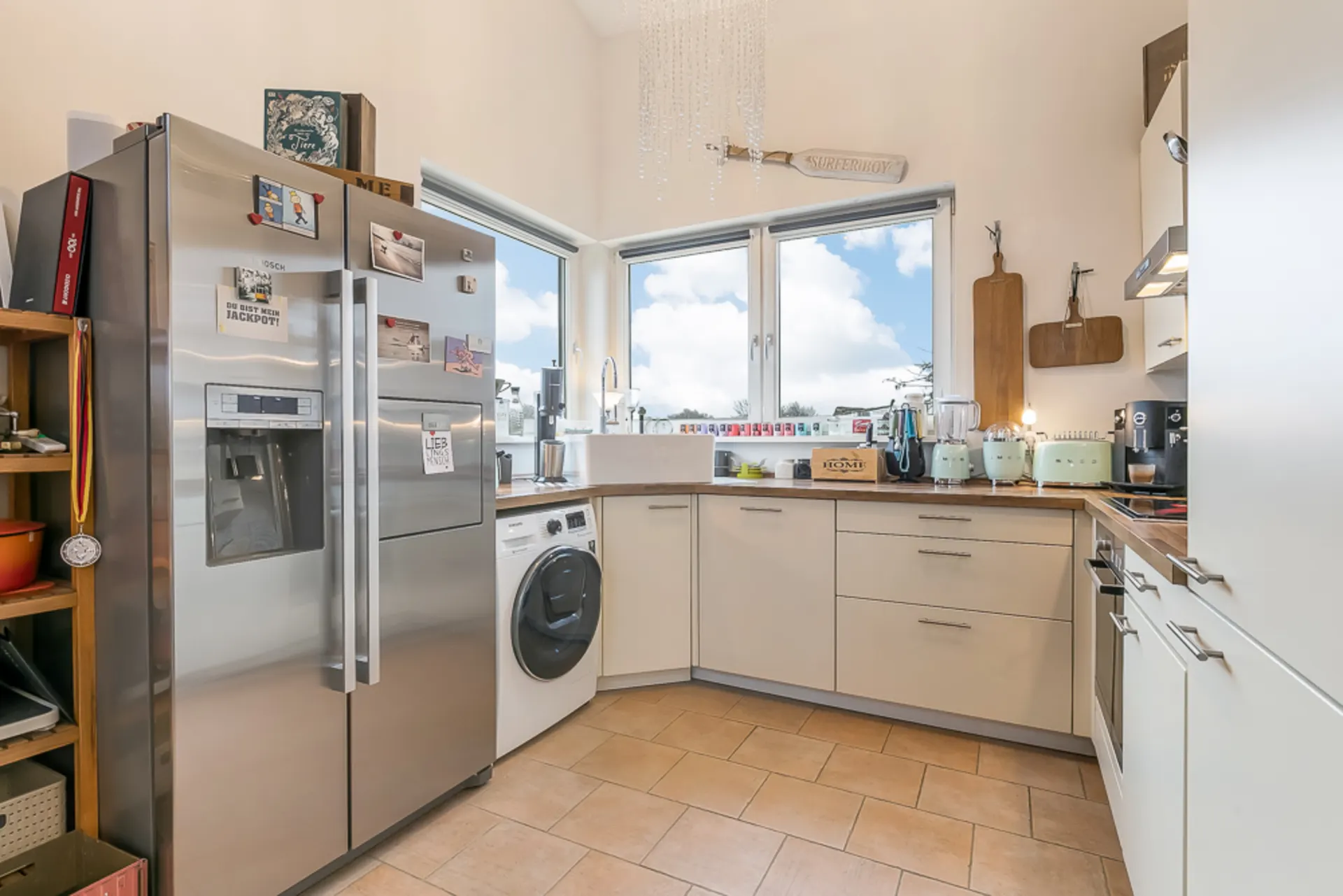 Helle Küche mit großem Kühlschrank, Waschmaschine, Spüle und Fenstern über der Arbeitsfläche.