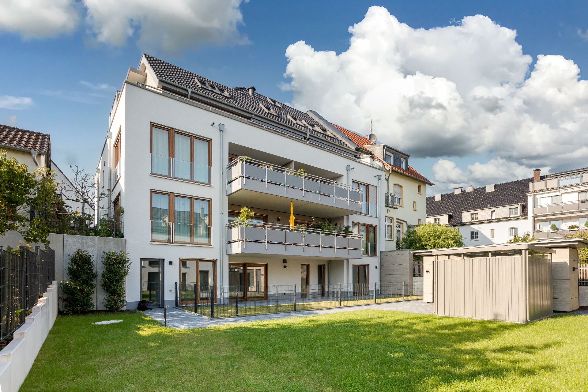 Modernes Wohngebäude mit mehreren Balkonen und gepflegtem Garten im Vordergrund.