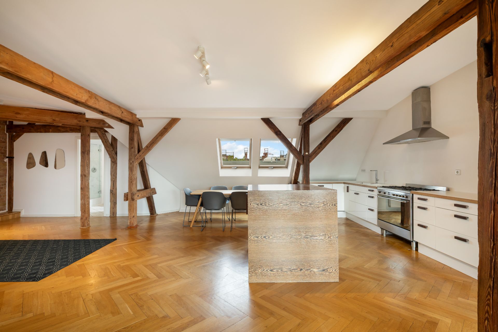 Helle Küche mit Holzbalken, Kochinsel, Essbereich und zwei Fenstern im Dachgeschoss.