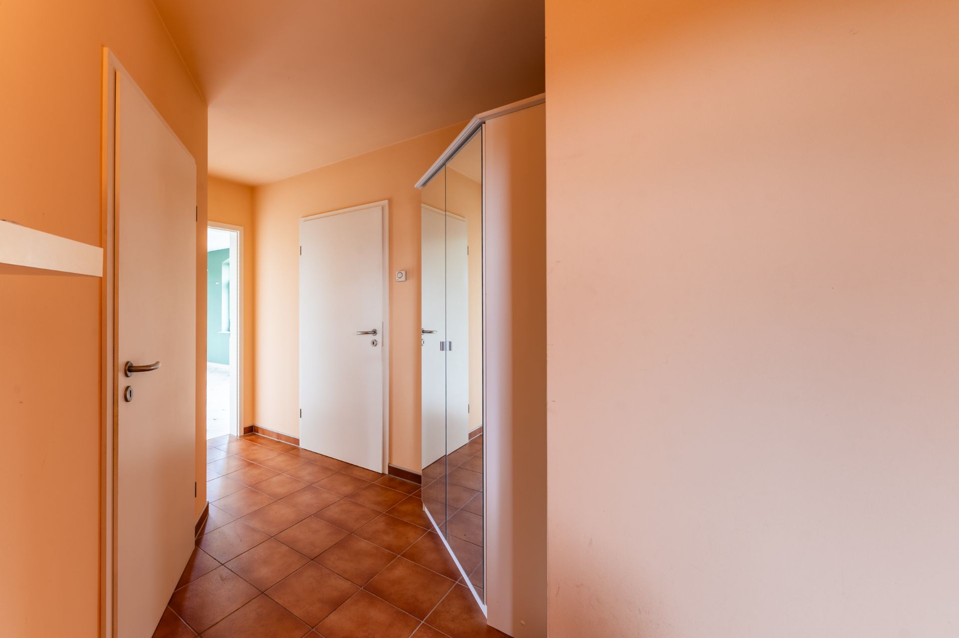Flur mit braunen Fliesen, weißen Türen und einem Spiegelschrank.