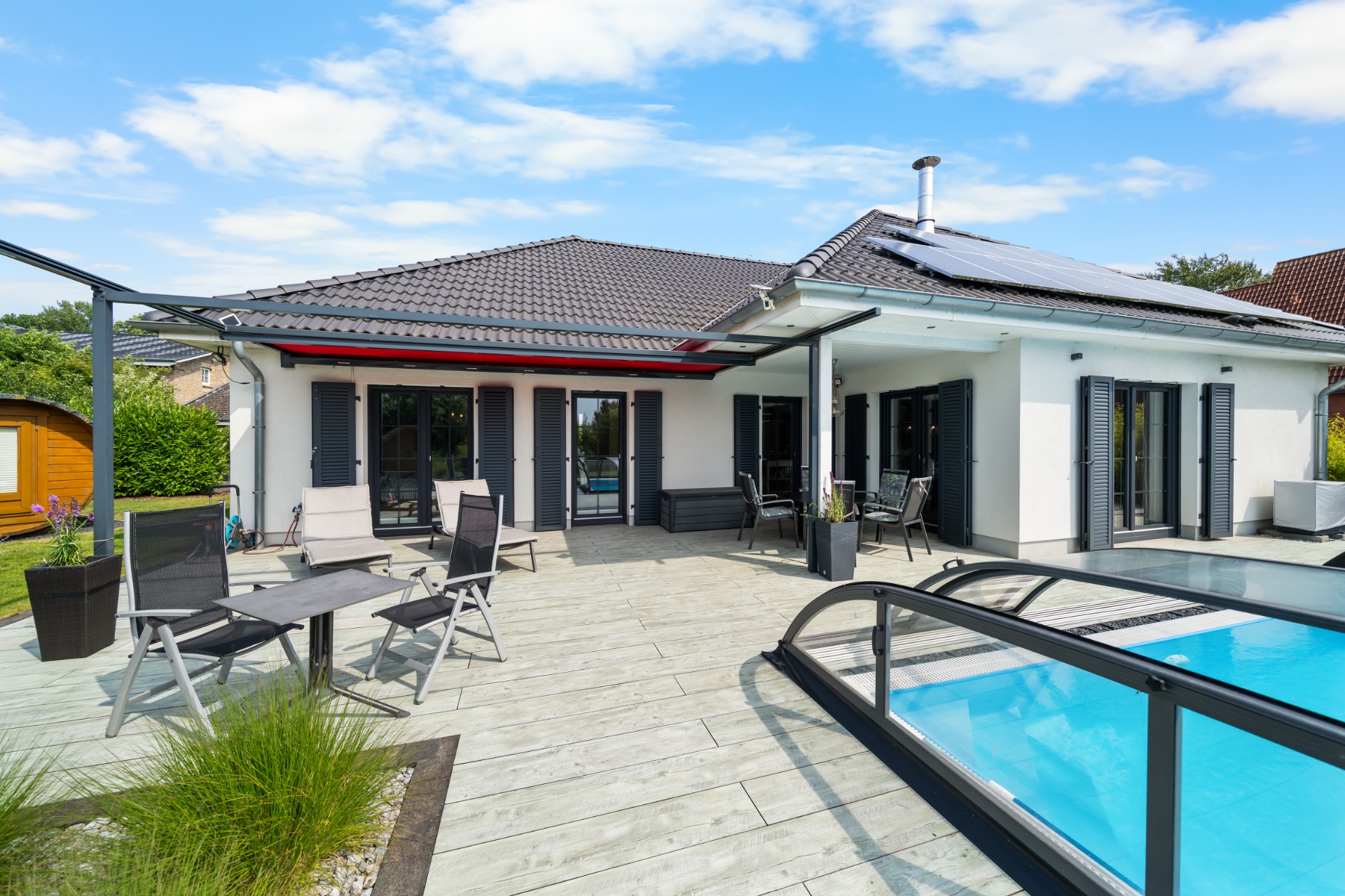 Moderne Terrasse mit Pool, Gartenmöbeln und großen Fenstern an einem Einfamilienhaus.