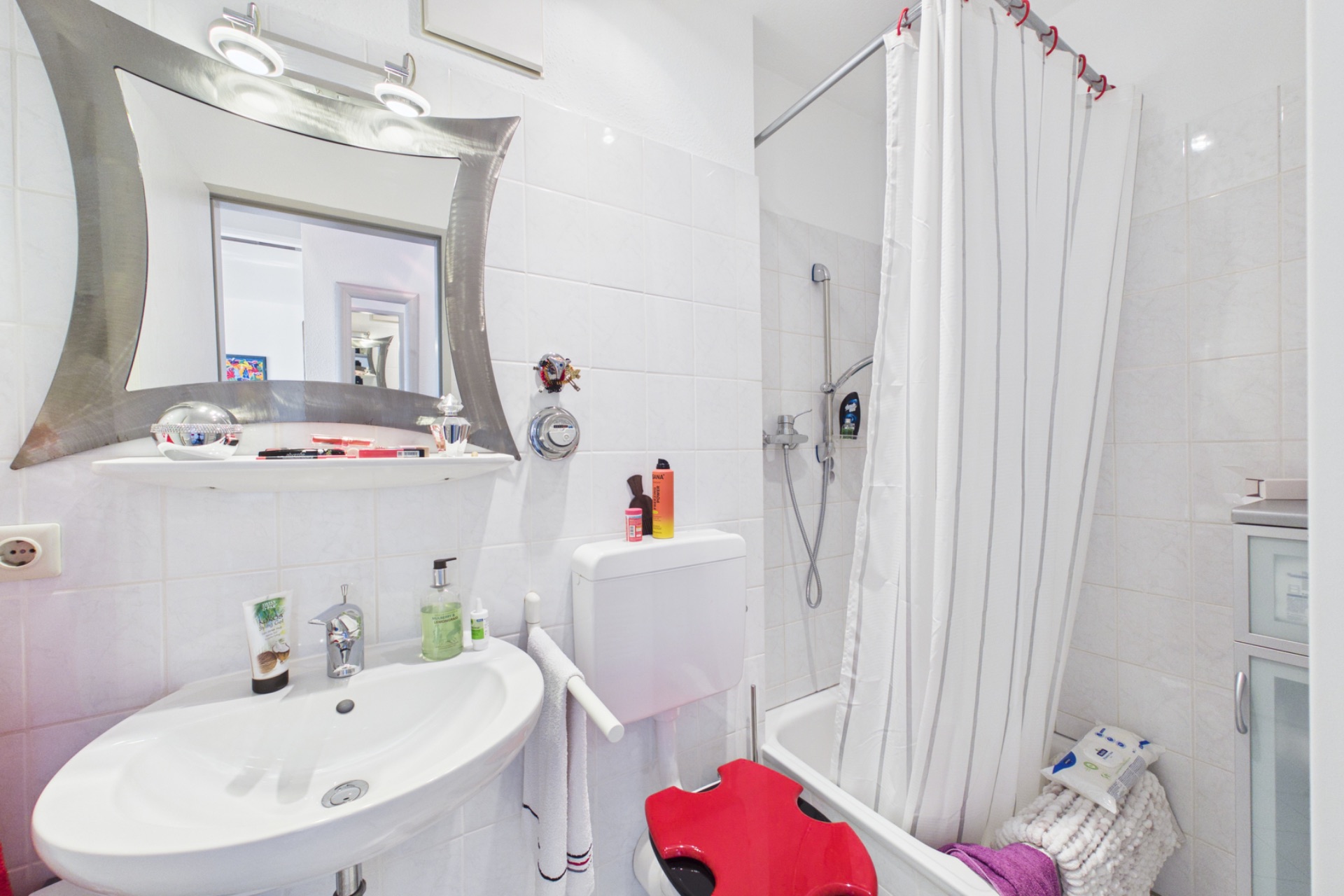 Kleines Badezimmer mit Waschbecken, Spiegel, Toilette und Dusche mit Duschvorhang.