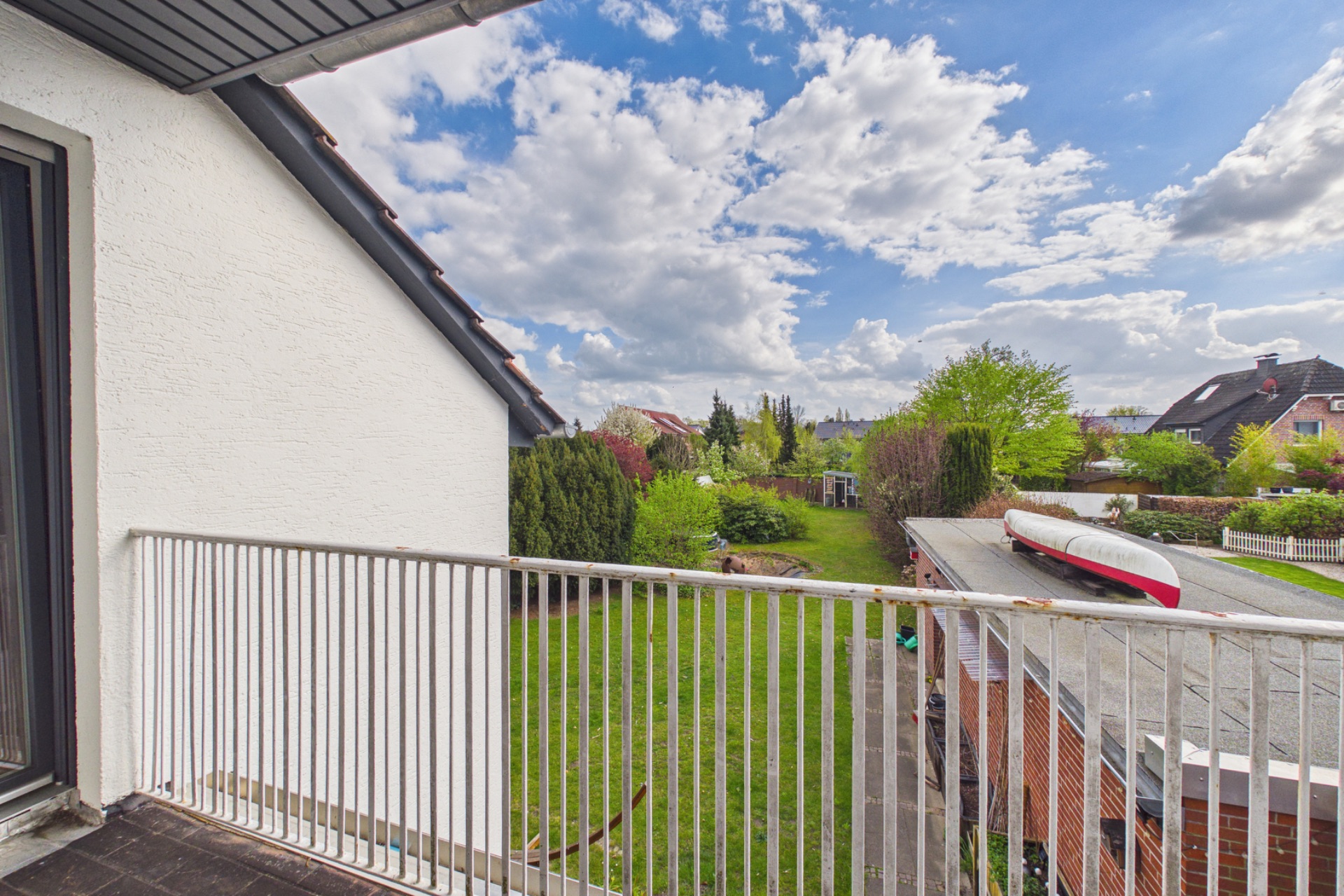 Blick von einem Balkon auf einen Garten mit Rasen, Bäumen und Garagendach.