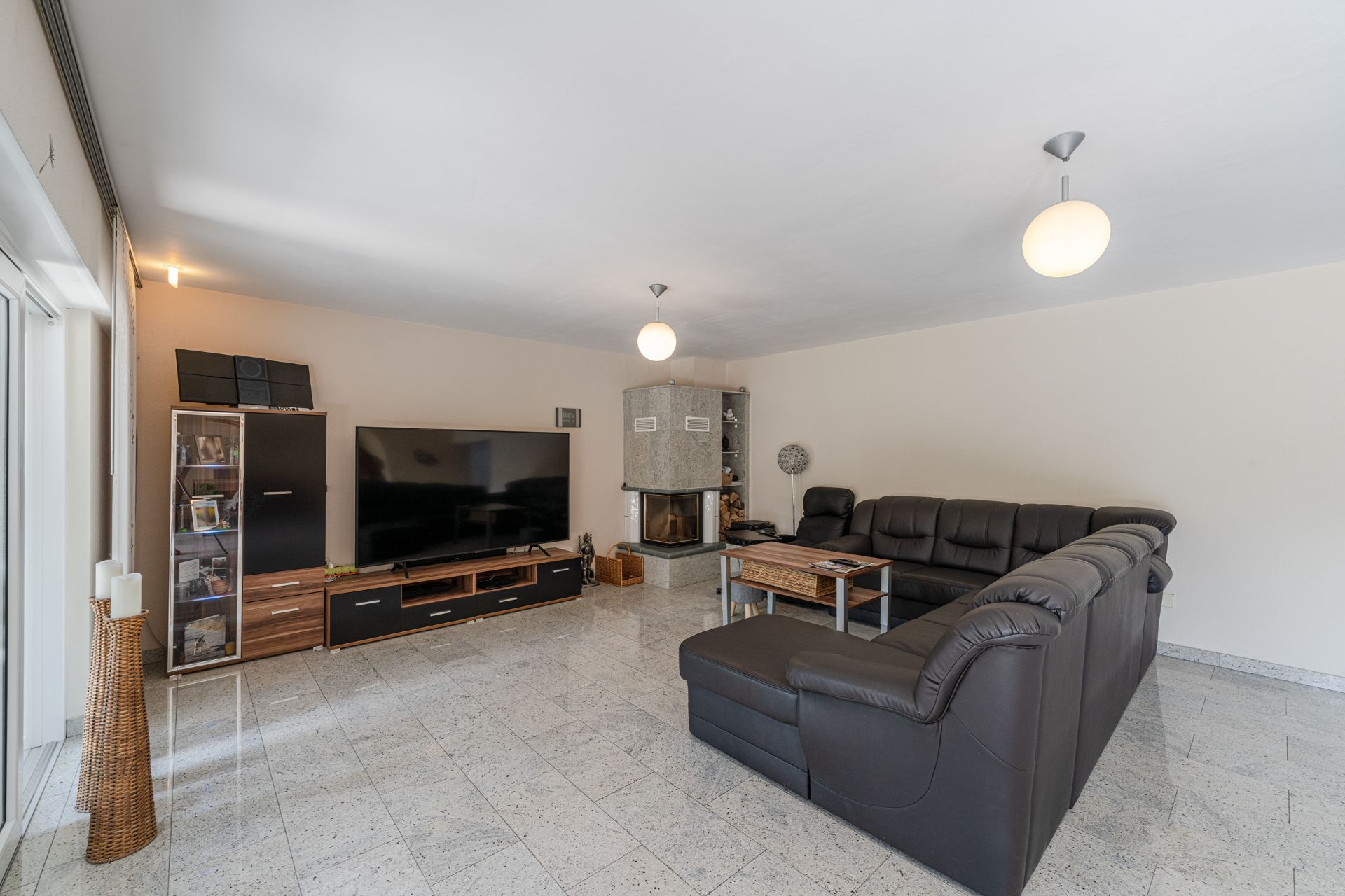 Helles Wohnzimmer mit großer schwarzer Eckcouch, Fernseher und Kamin.
