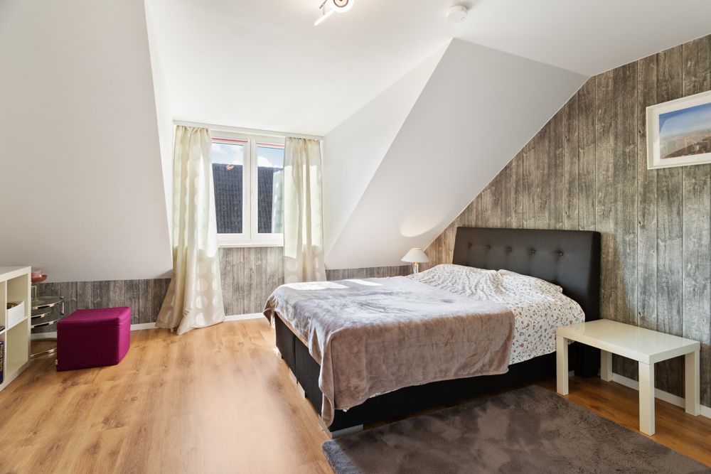Helles Schlafzimmer mit Doppelbett, Holzboden, Dachschräge und Fenster mit Vorhängen.